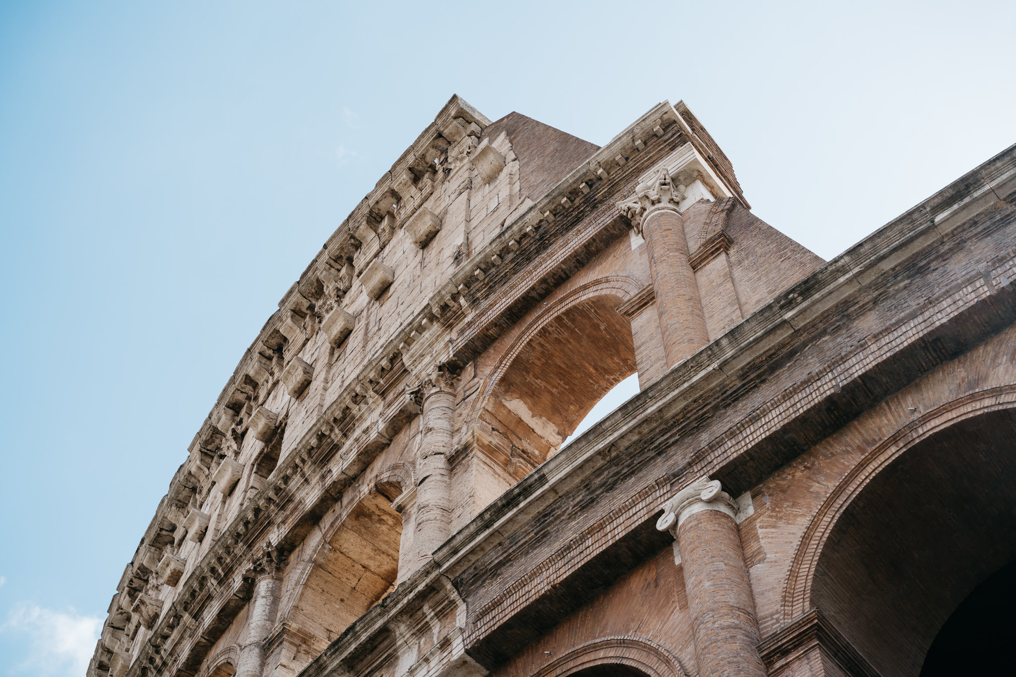 Low-angle view of the Colosseum's exterior, showcasing its stone arches and columns against a clear sky.