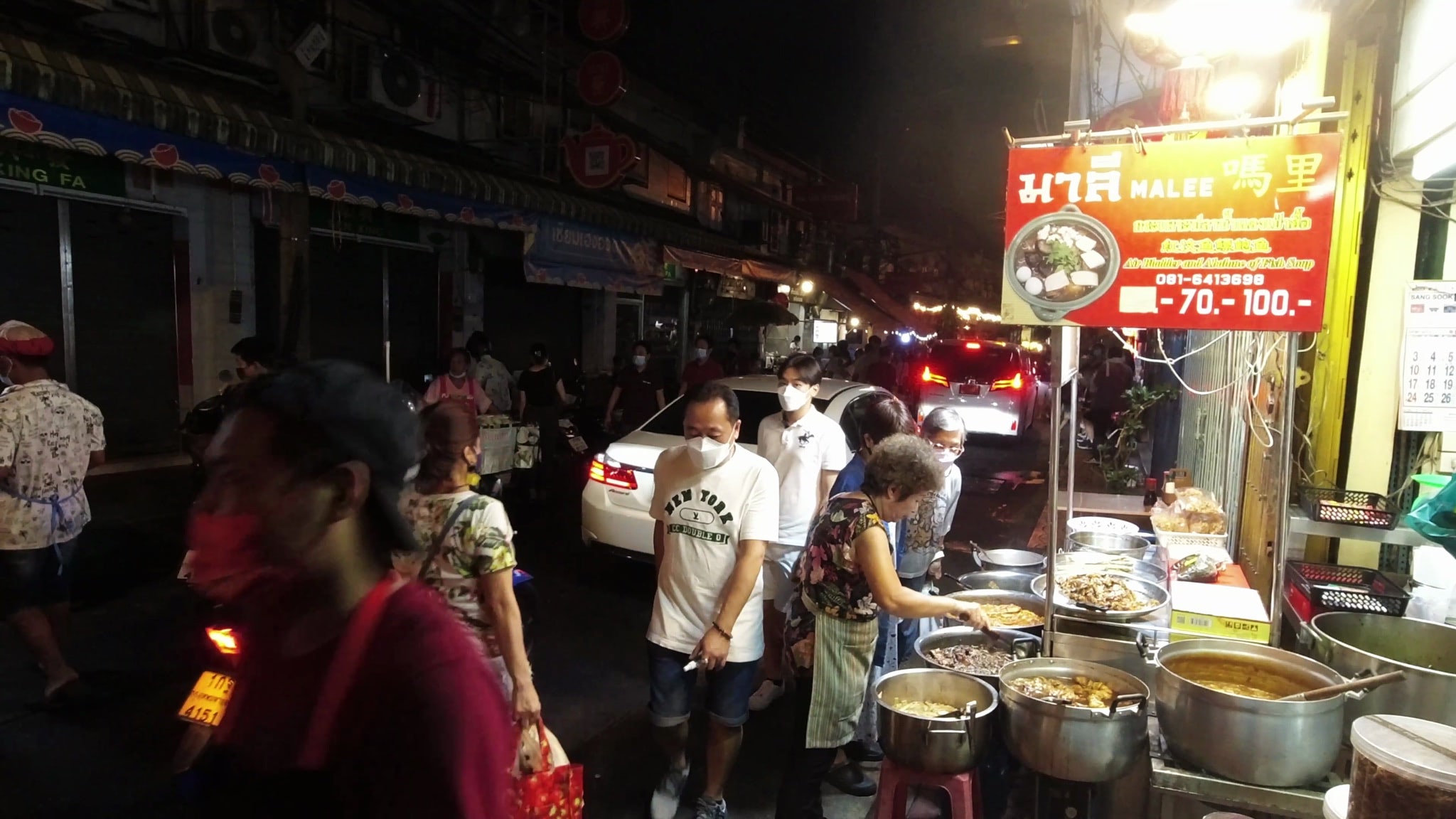 Bangkok night market food stall serving food to masked customers.