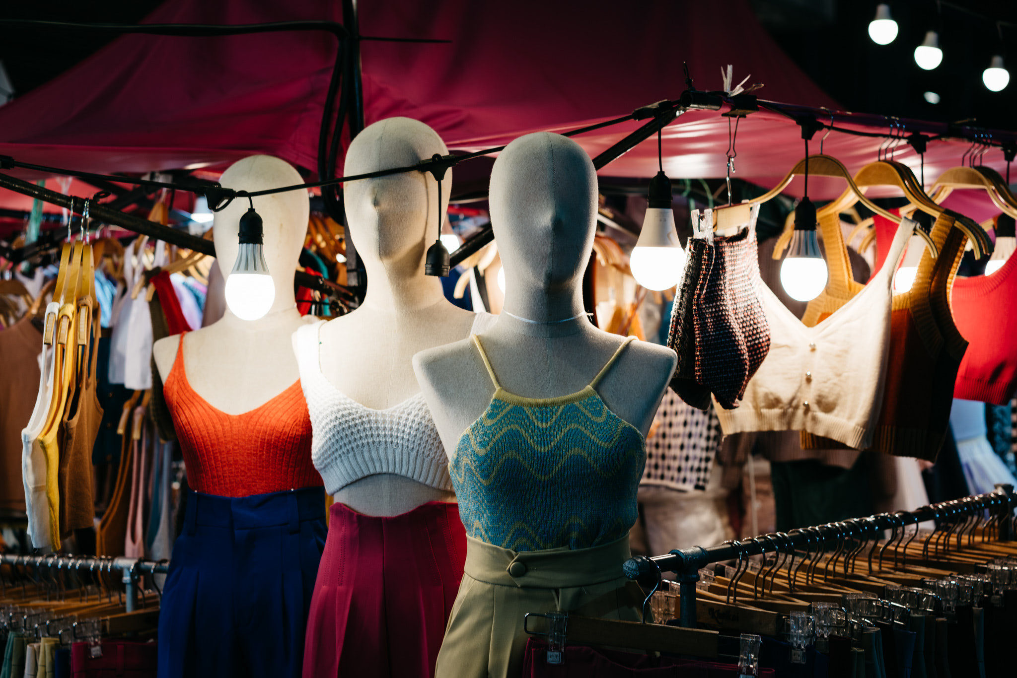 Three mannequins display women's clothing at a night market.