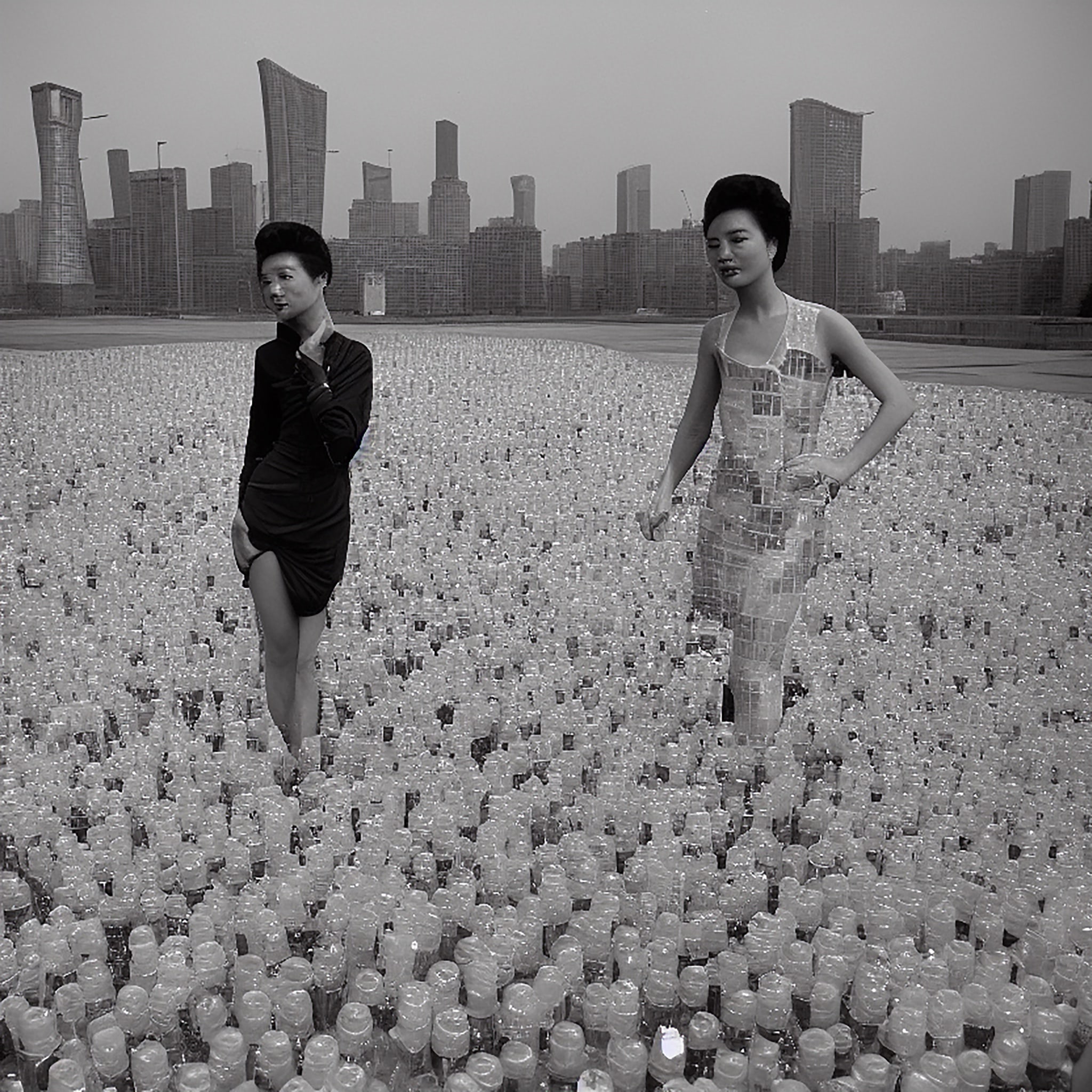 Two women in dresses made of plastic bottles stand in front of a city skyline.
