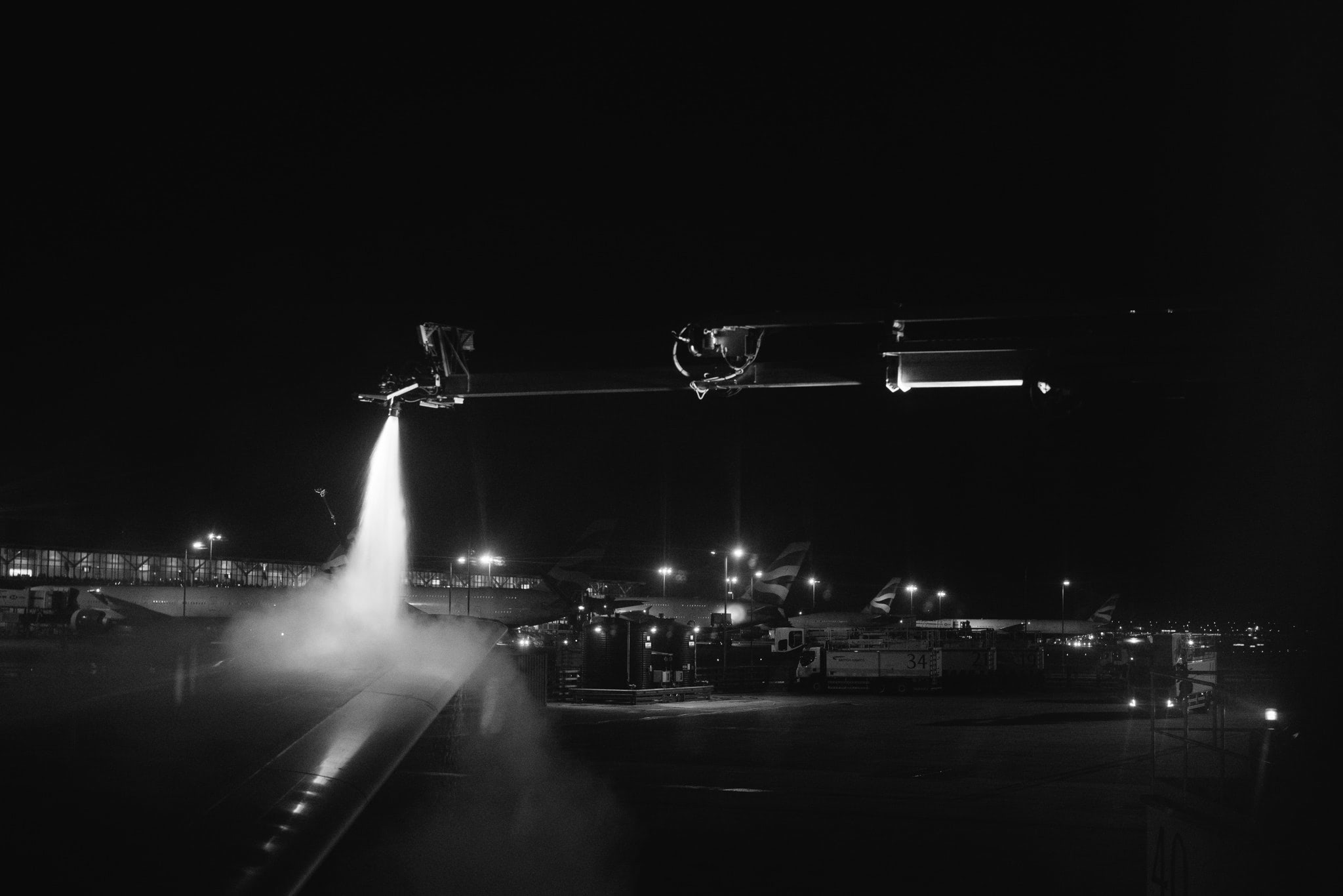 Black and white photo of a British Airways plane being de-iced at night.