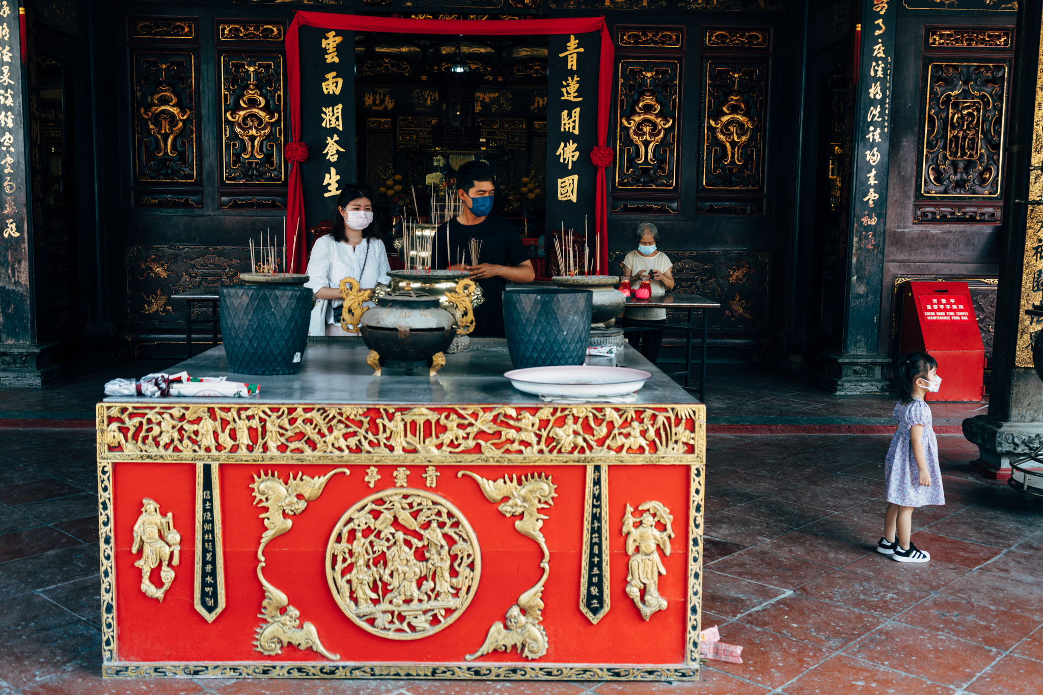 People wearing masks pray at an ornate altar in a Chinese temple.