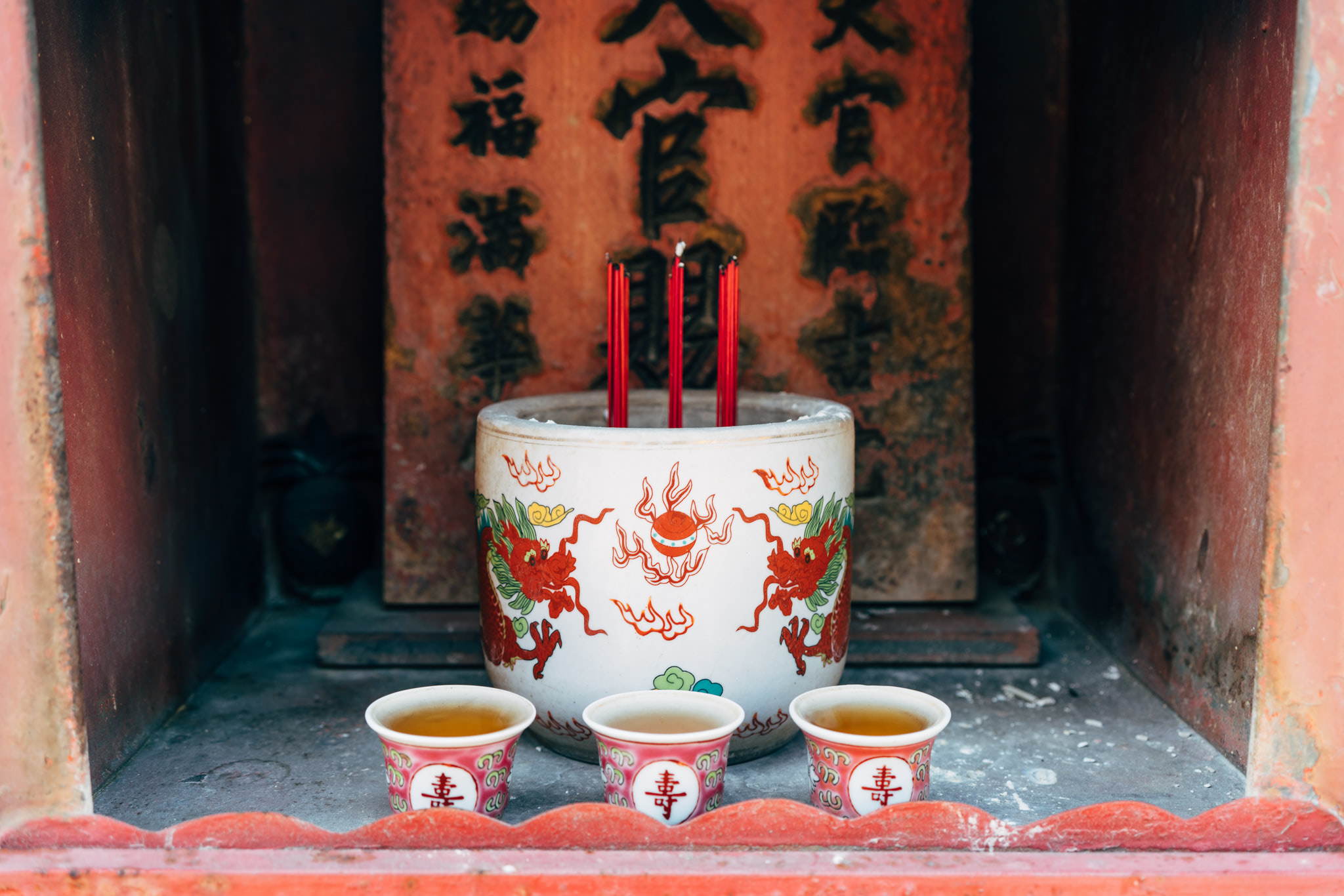 Incense burning in a dragon-decorated urn with teacups in a Chinese temple alcove.