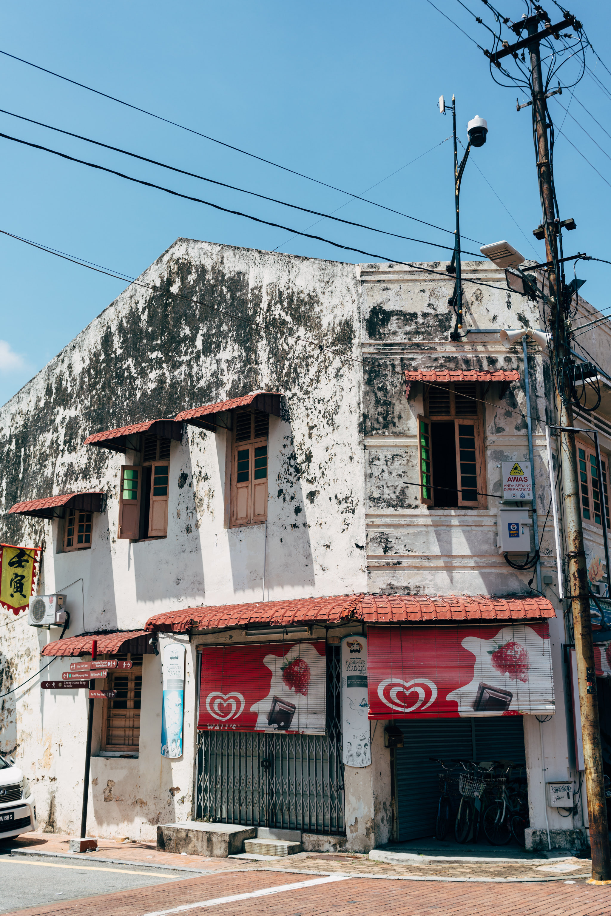Weathered white building with red awnings, Walls ice cream advertisement, and bicycles parked underneath.