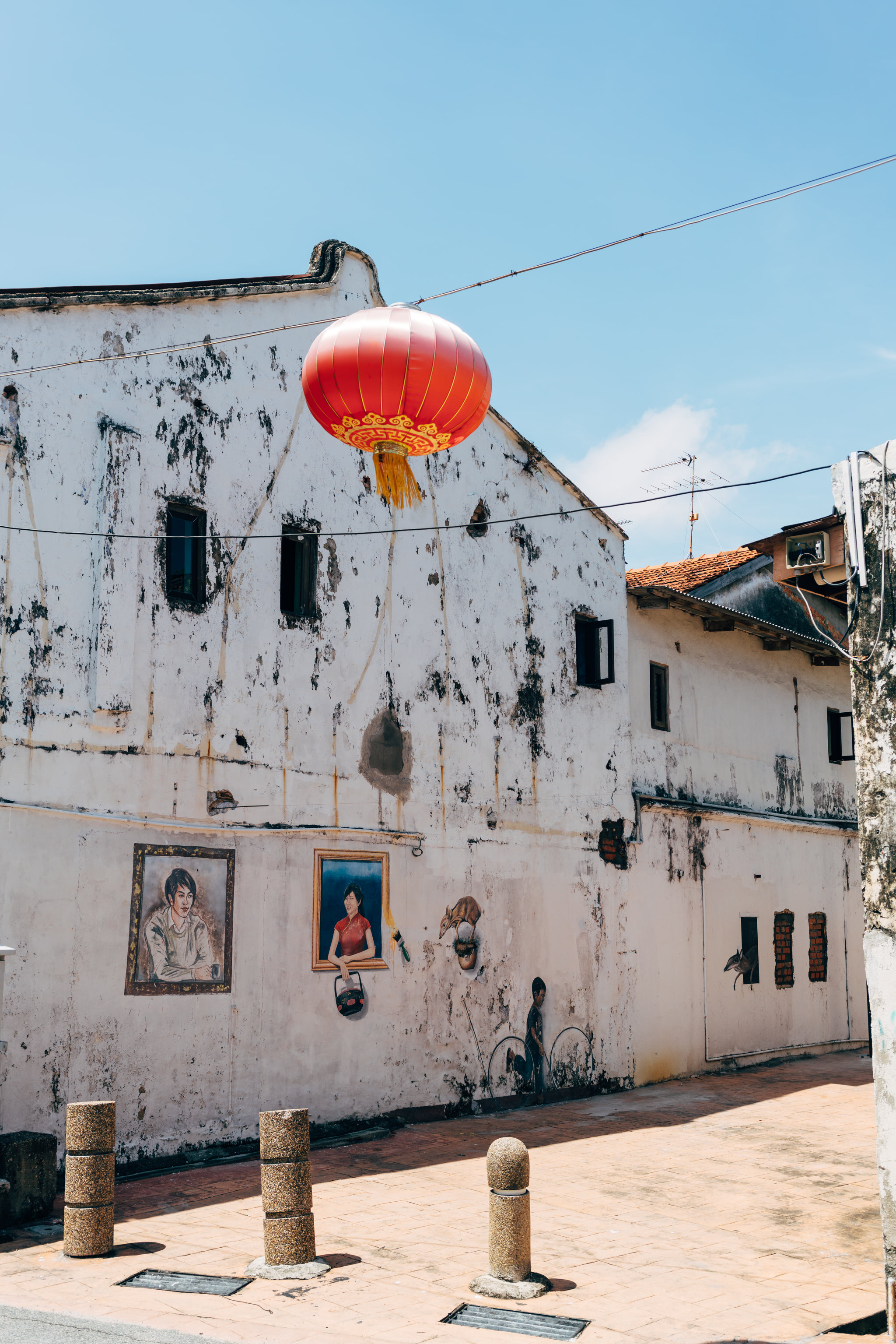 Red lantern hanging above street art on weathered building in Malacca, Malaysia.