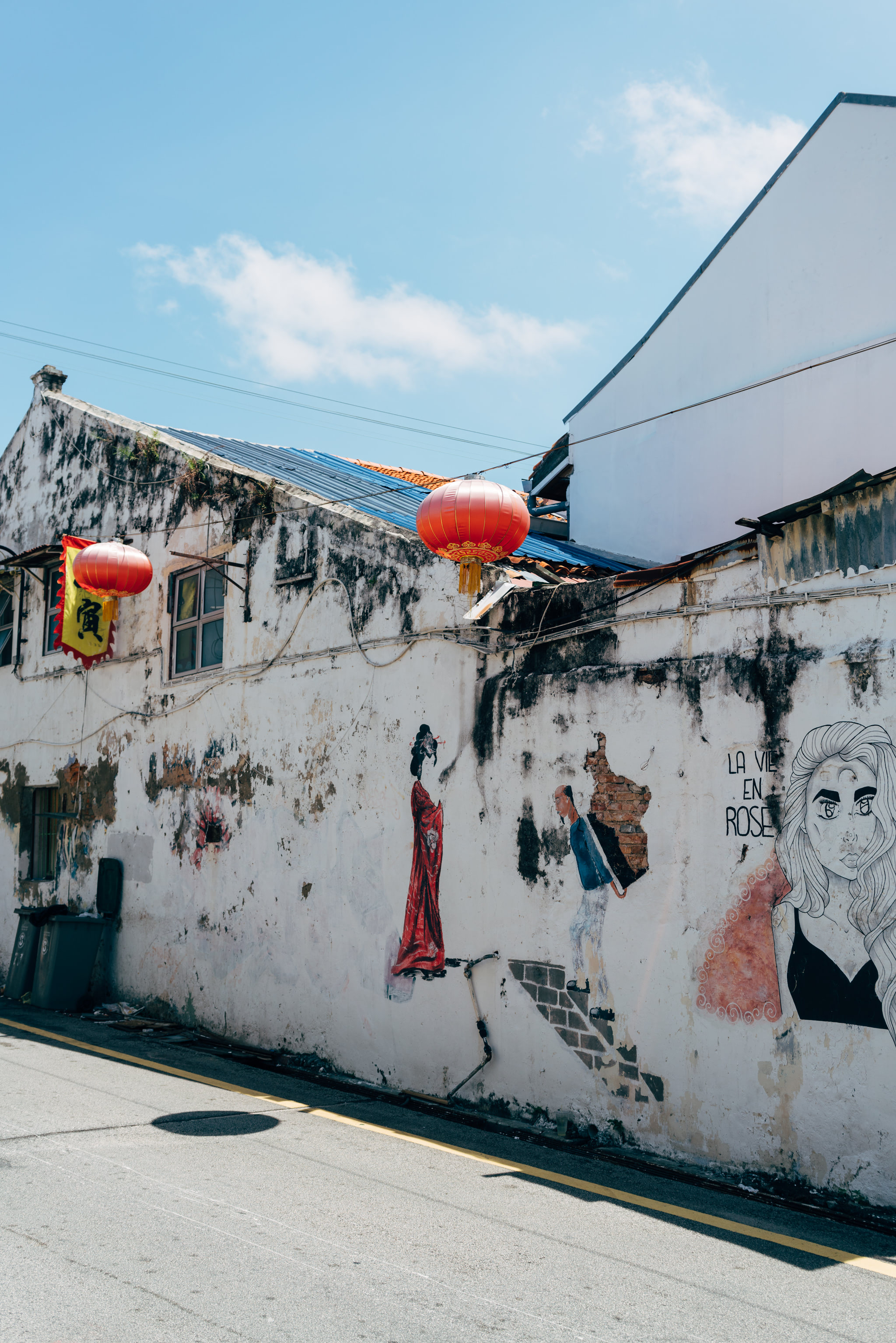 Street art on a weathered building in Malacca, Malaysia, with red Chinese lanterns.