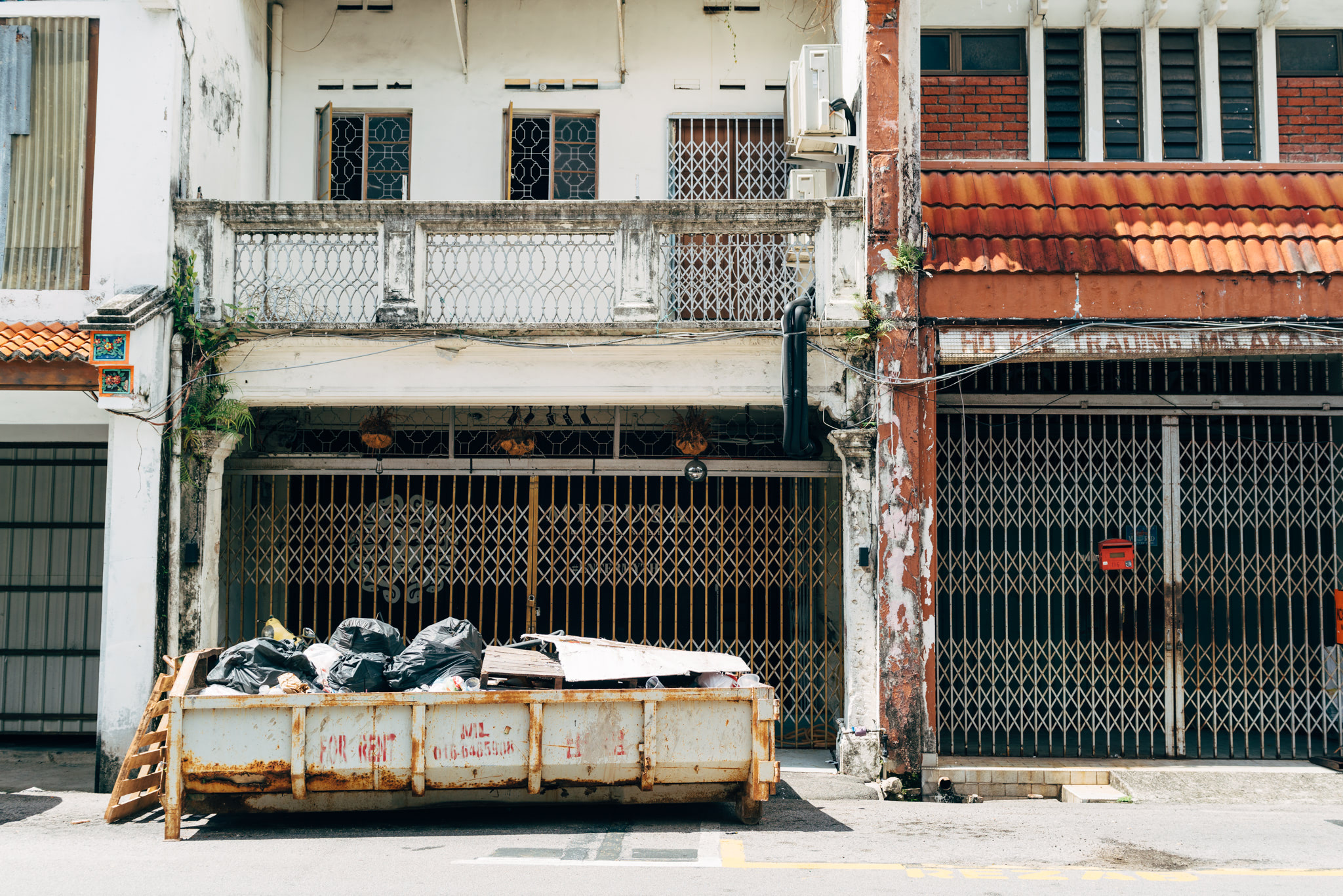 Dumpster overflowing with trash in front of aged buildings in Malacca, Malaysia.