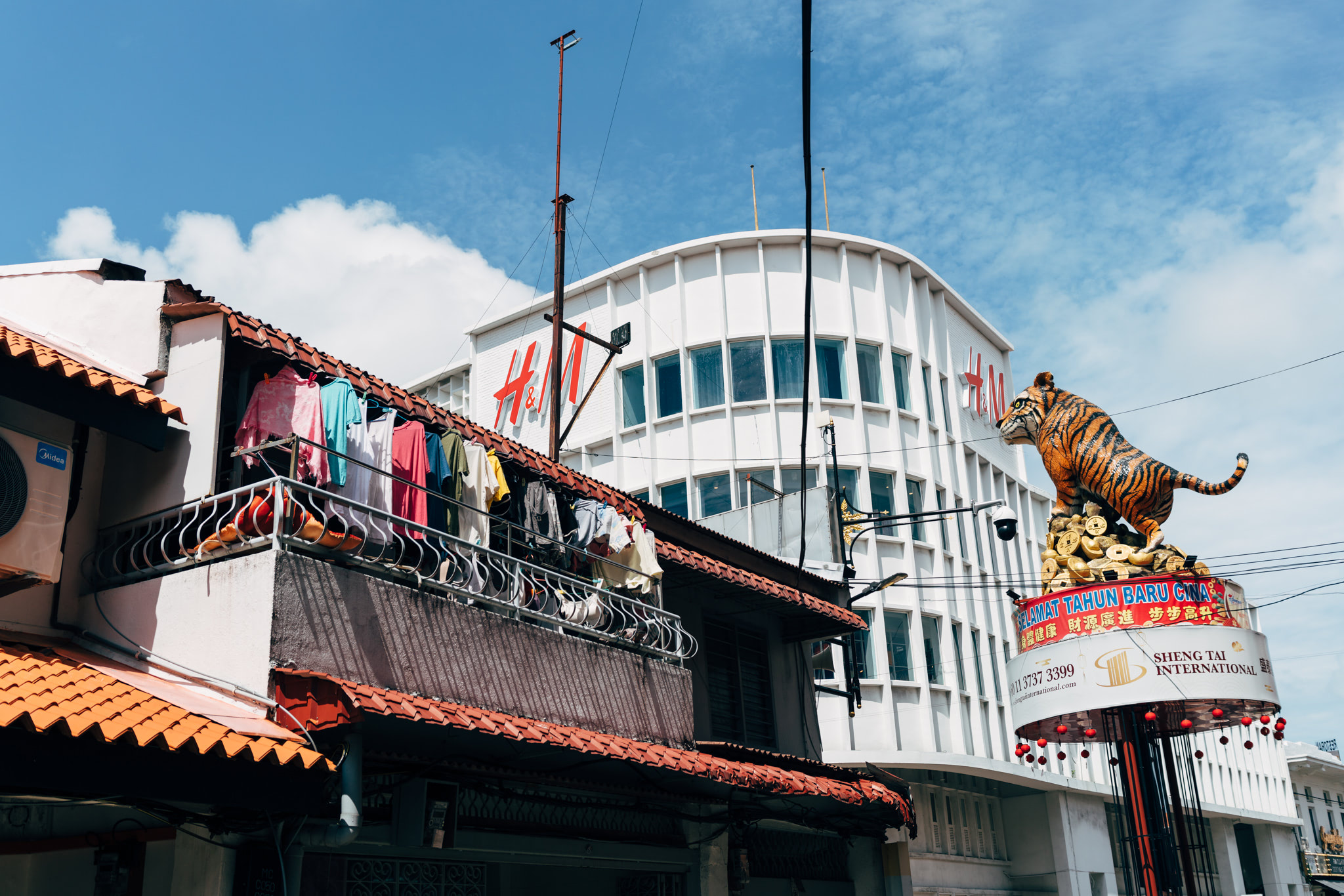 Malacca street scene with clothes drying on a balcony, an H&M building, and a large tiger statue.