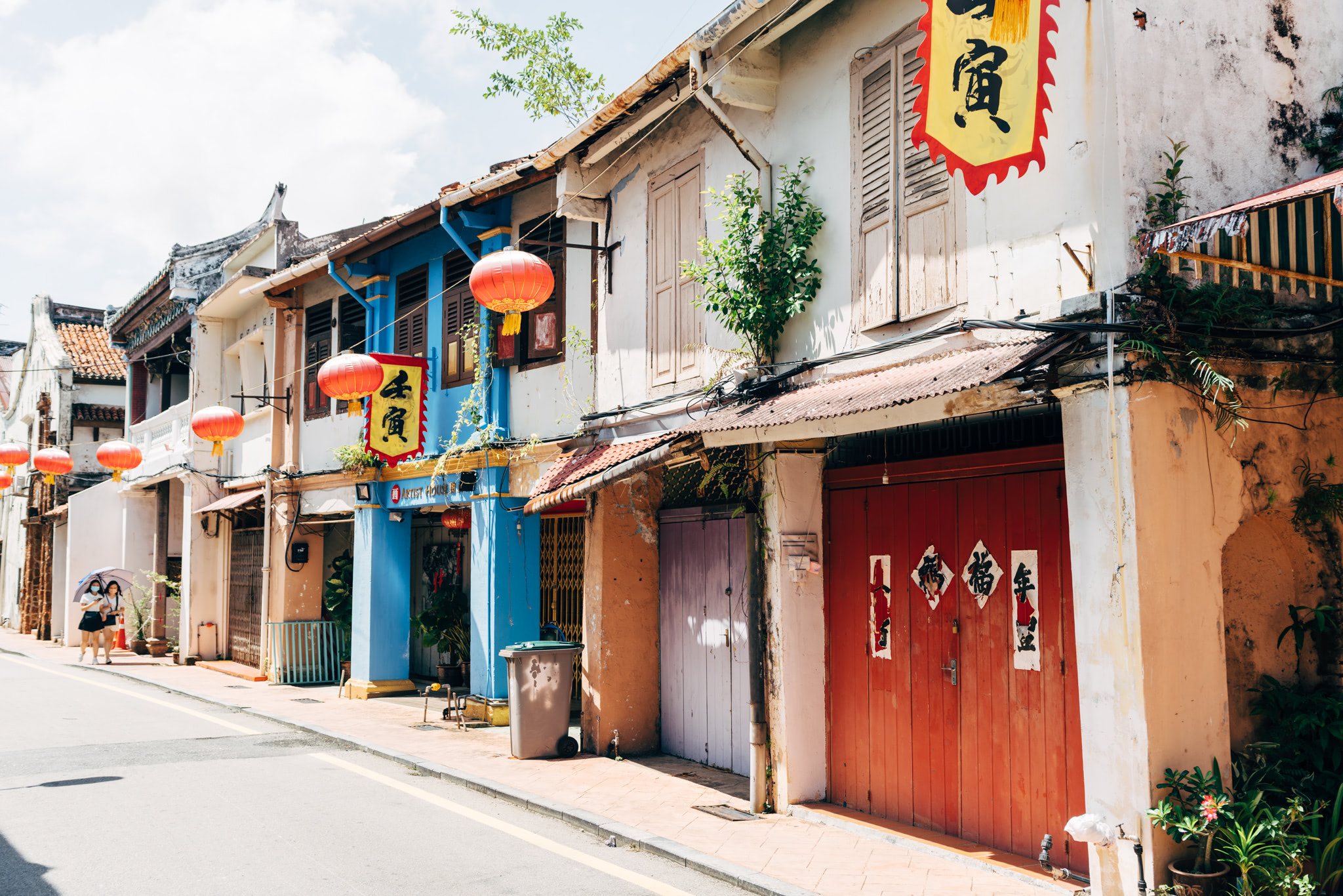 Street scene in Malacca, Malaysia, featuring colorful shophouses with red lanterns and Chinese characters.