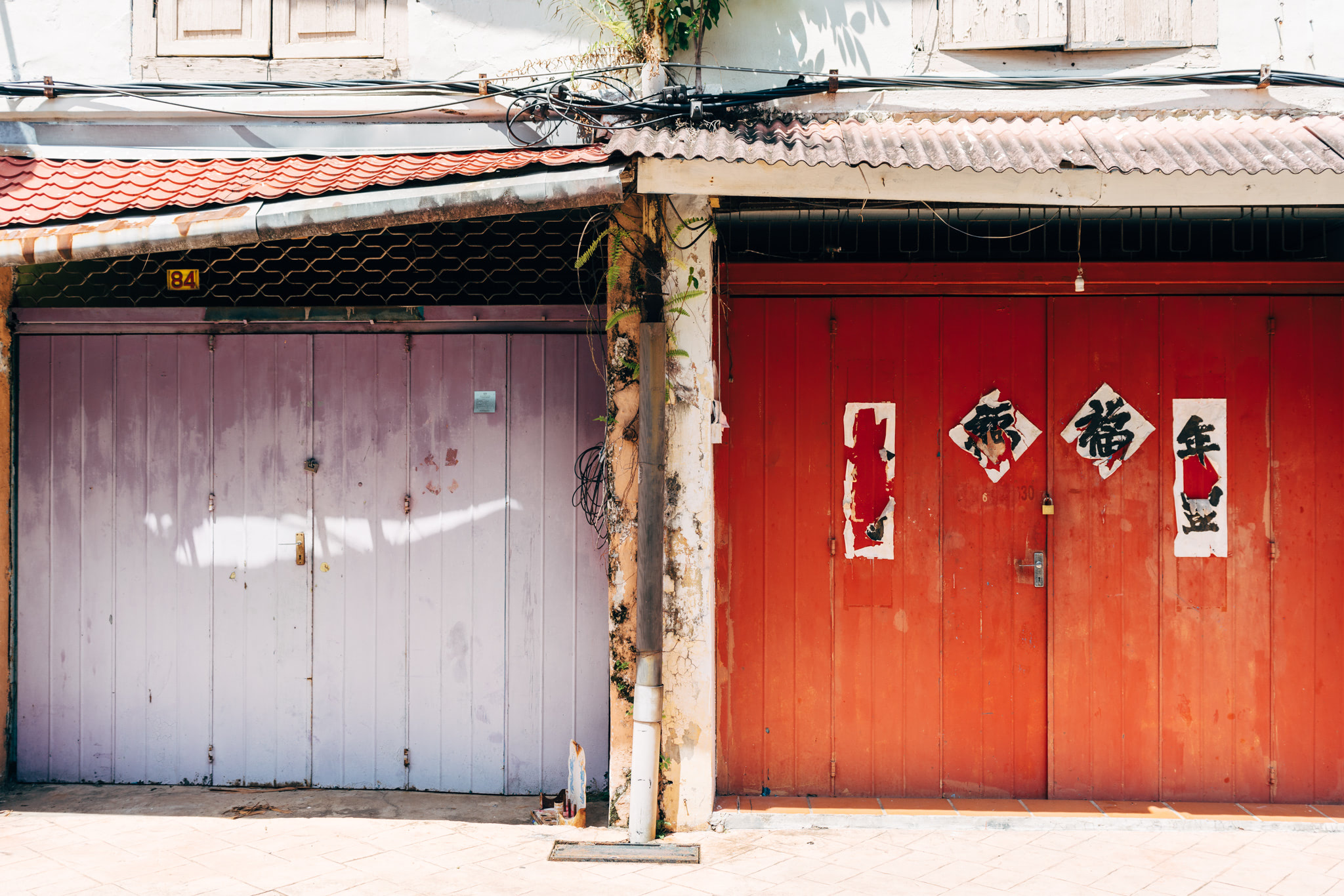 Two adjacent shopfronts in Malacca, Malaysia; one with lavender doors and the other with red doors displaying Chinese characters.