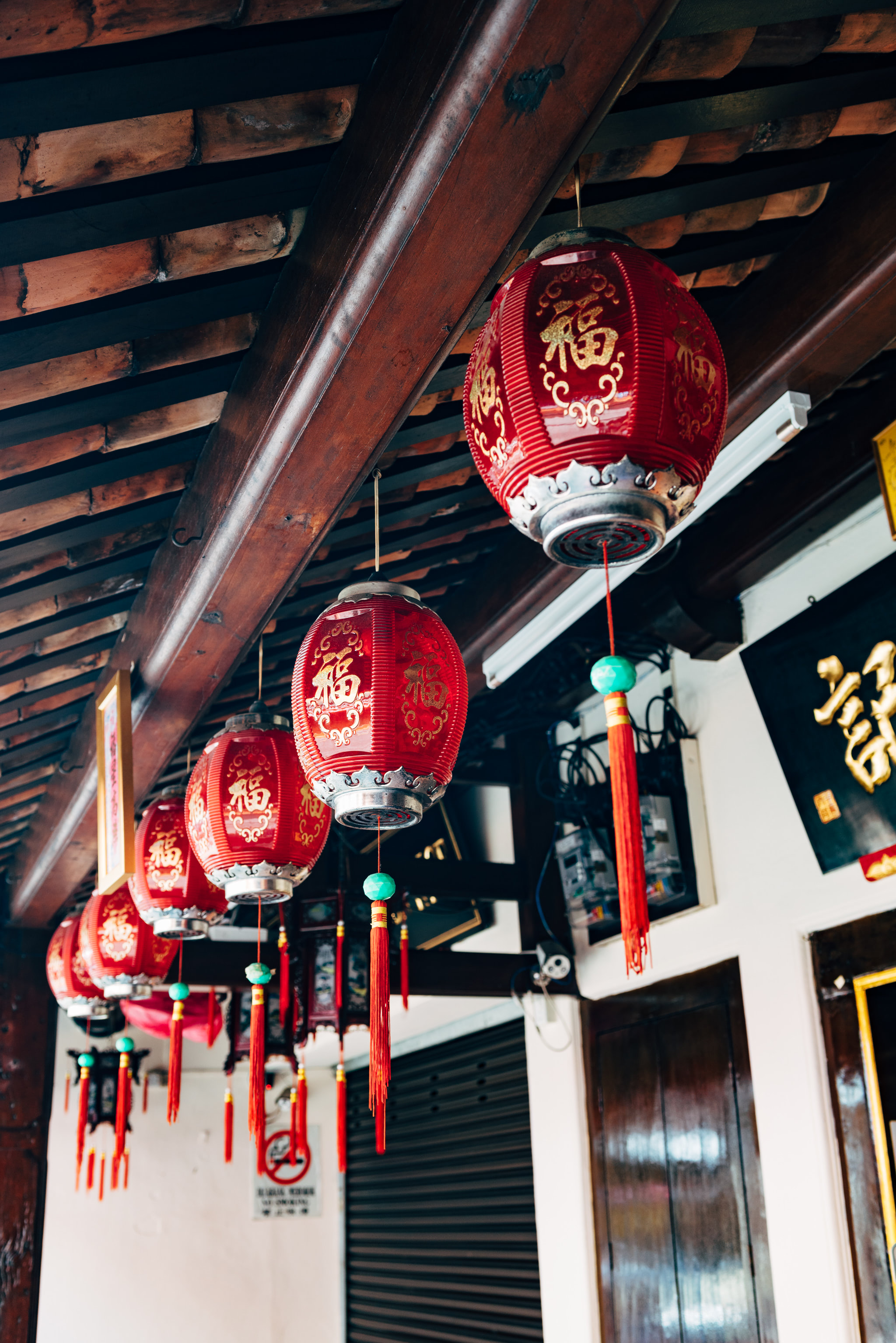 Red Chinese lanterns with gold characters hanging from a wooden ceiling.