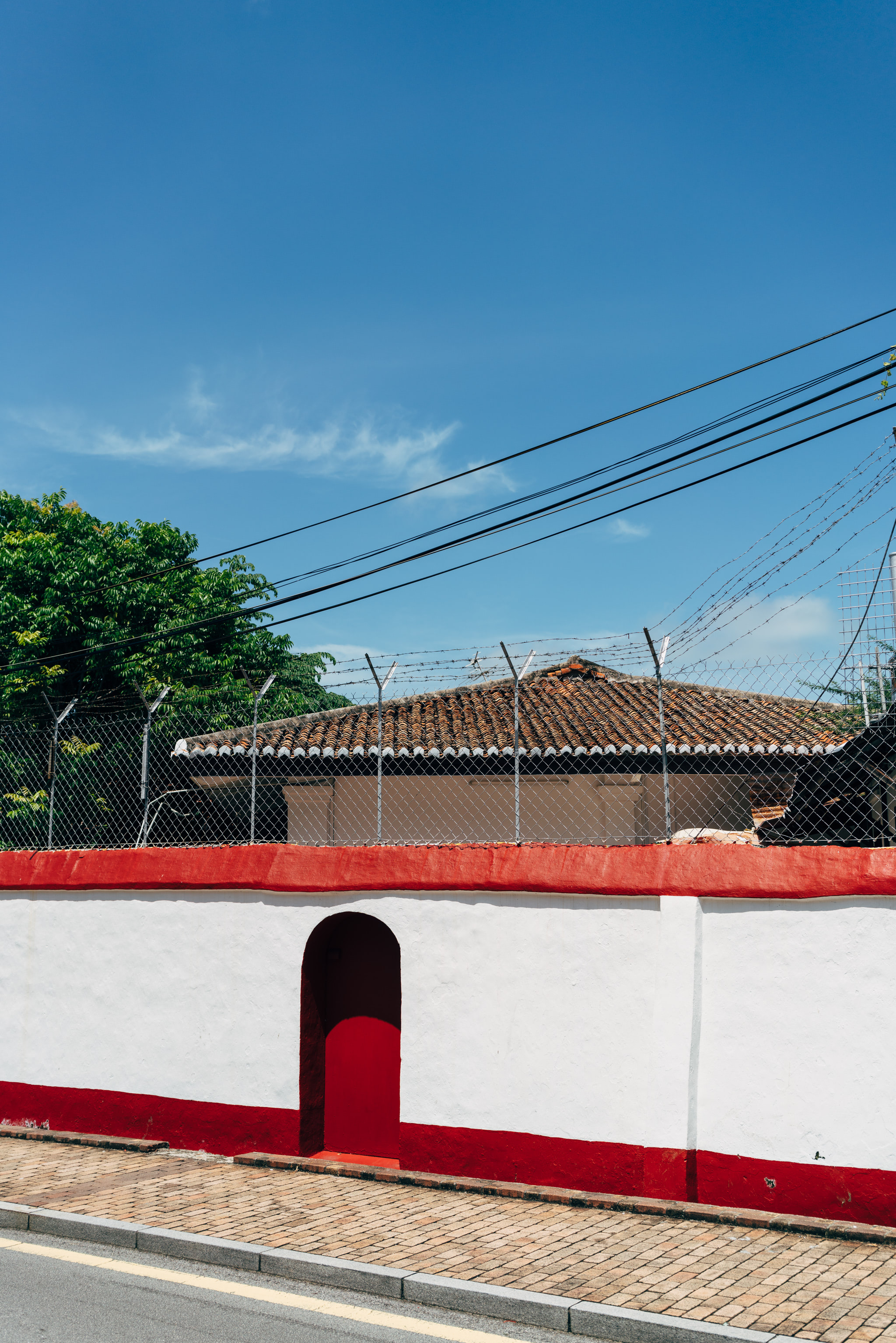 Red and white walled building with barbed wire fence and red door in Malacca, Malaysia.