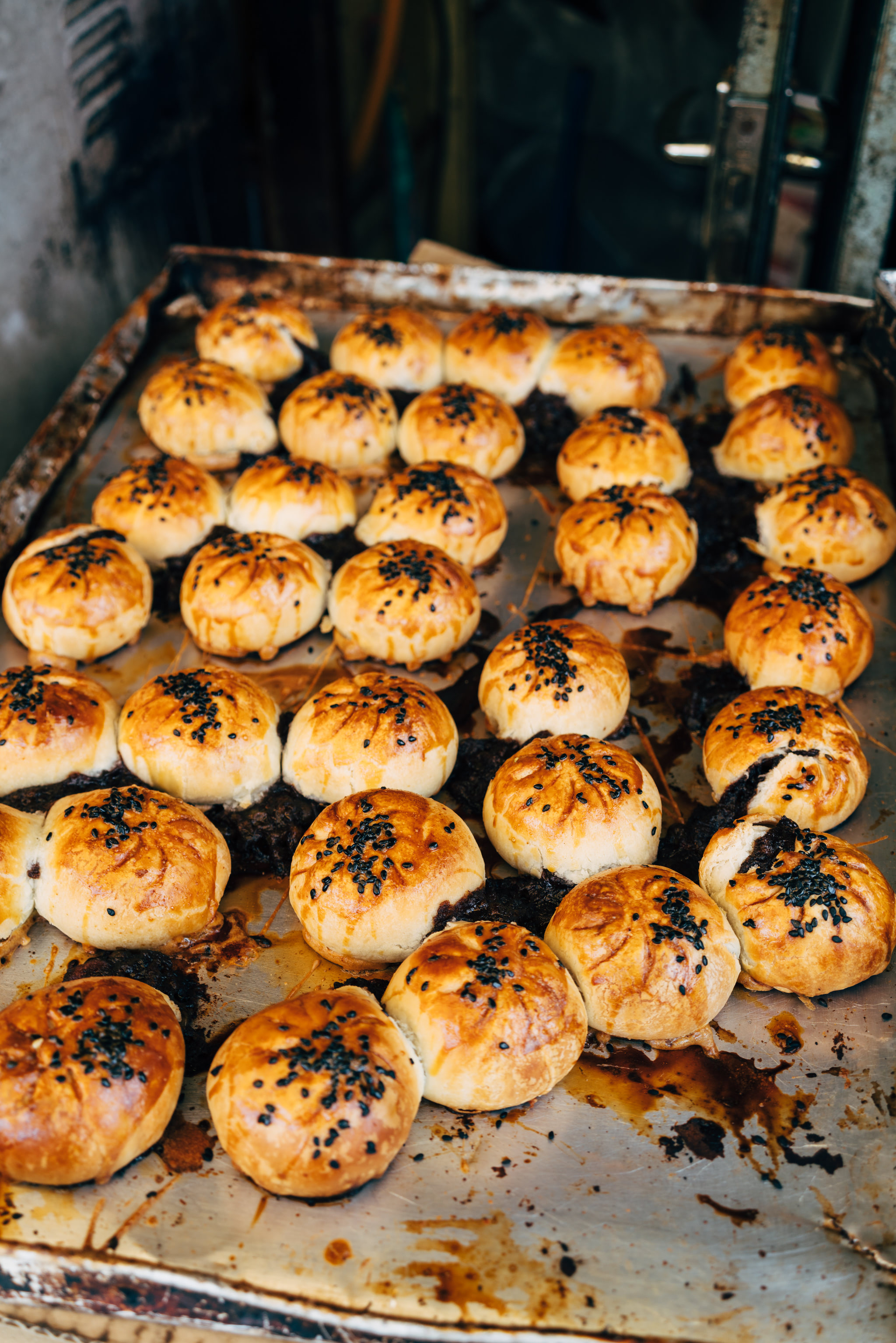 Baked buns with black sesame seeds on a baking sheet.