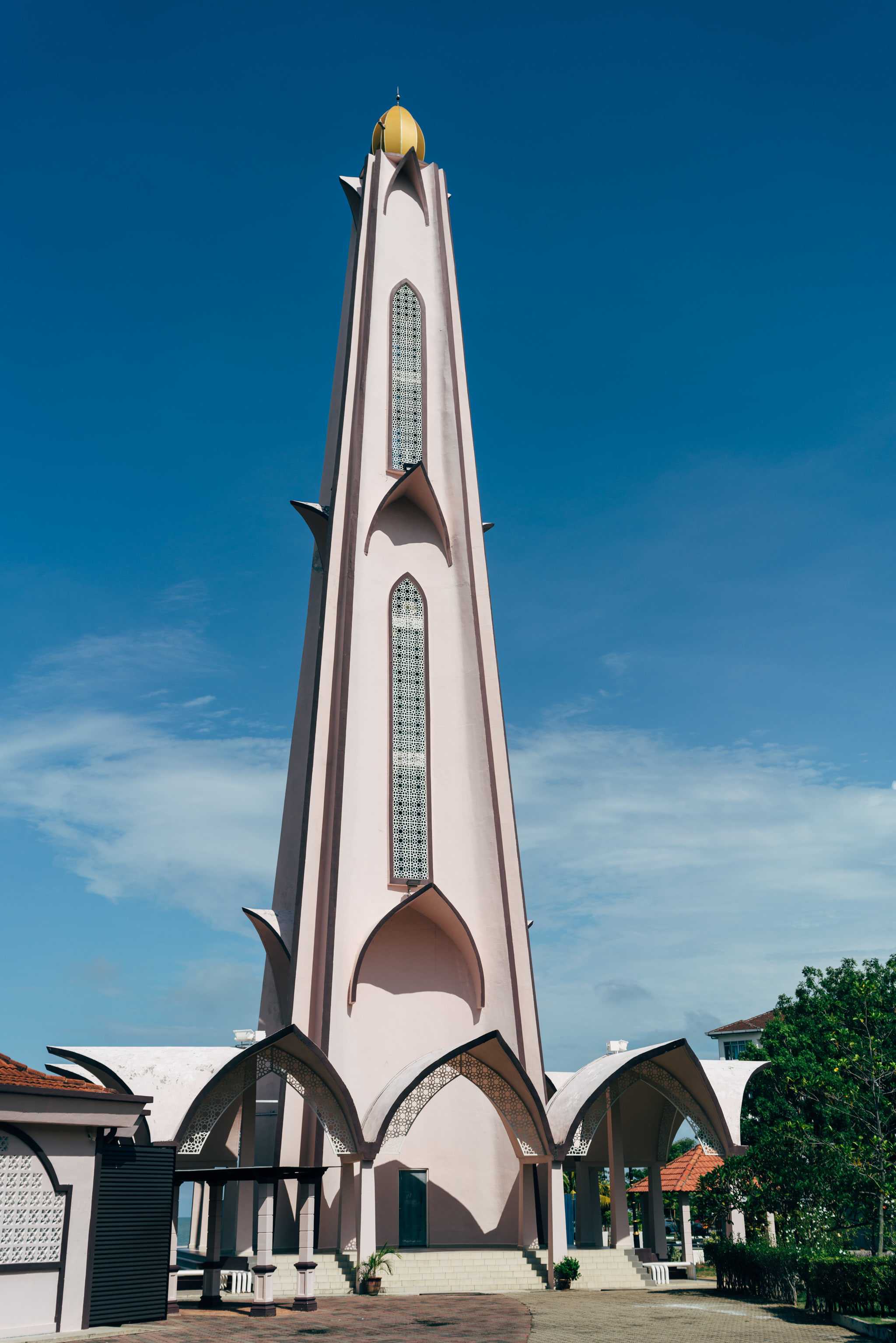 Tall pink minaret of the Straits Mosque in Malacca, Malaysia, against a blue sky.