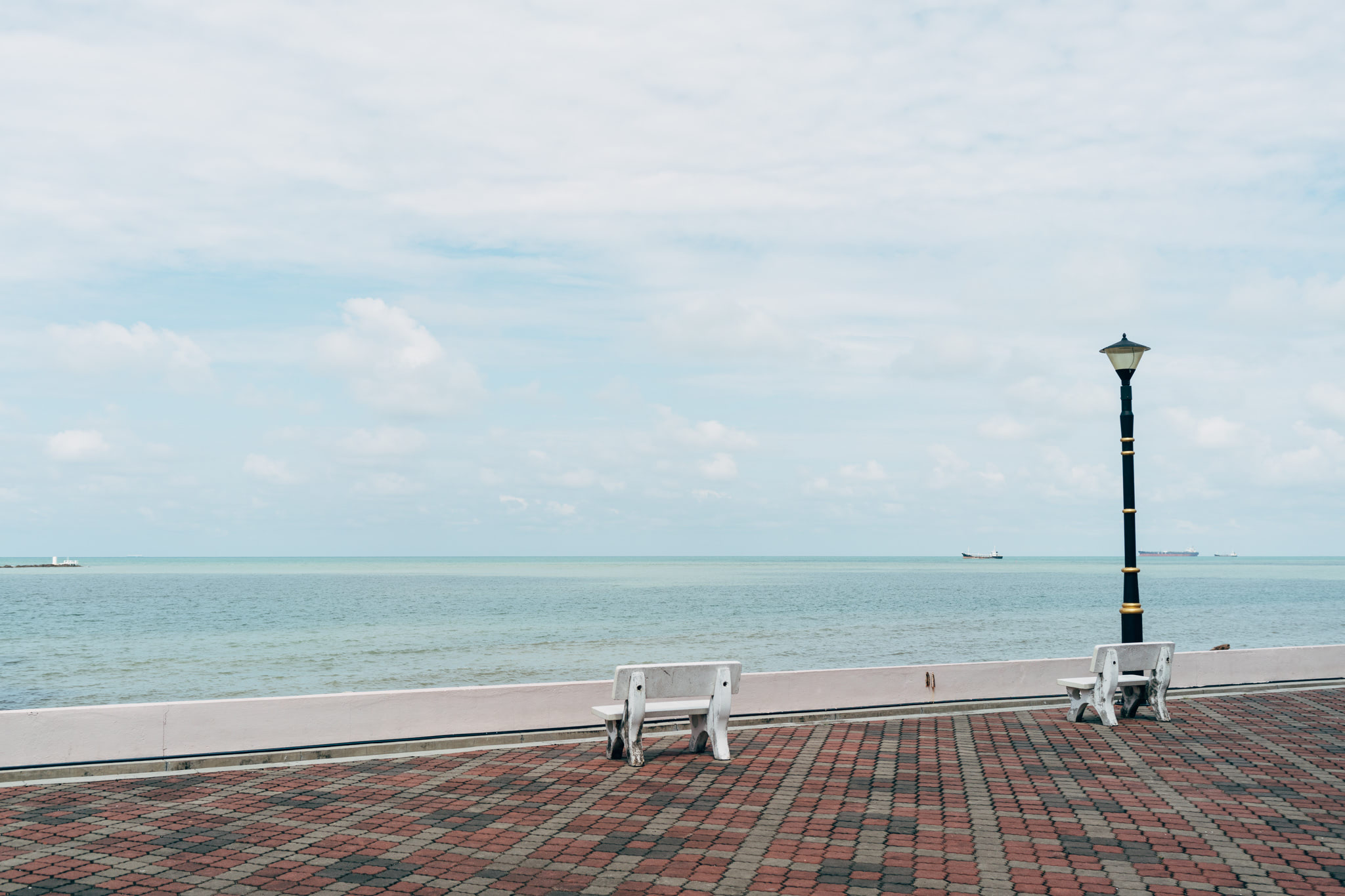Two empty benches on a brick paved walkway overlooking the Straits of Melaka.