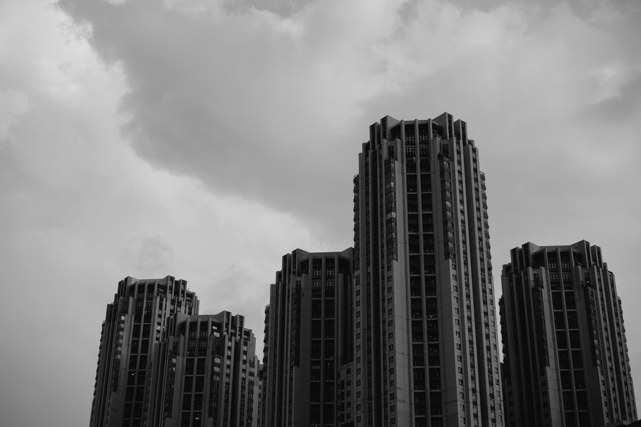 Black and white photo of three tall, slender residential buildings against a cloudy sky.