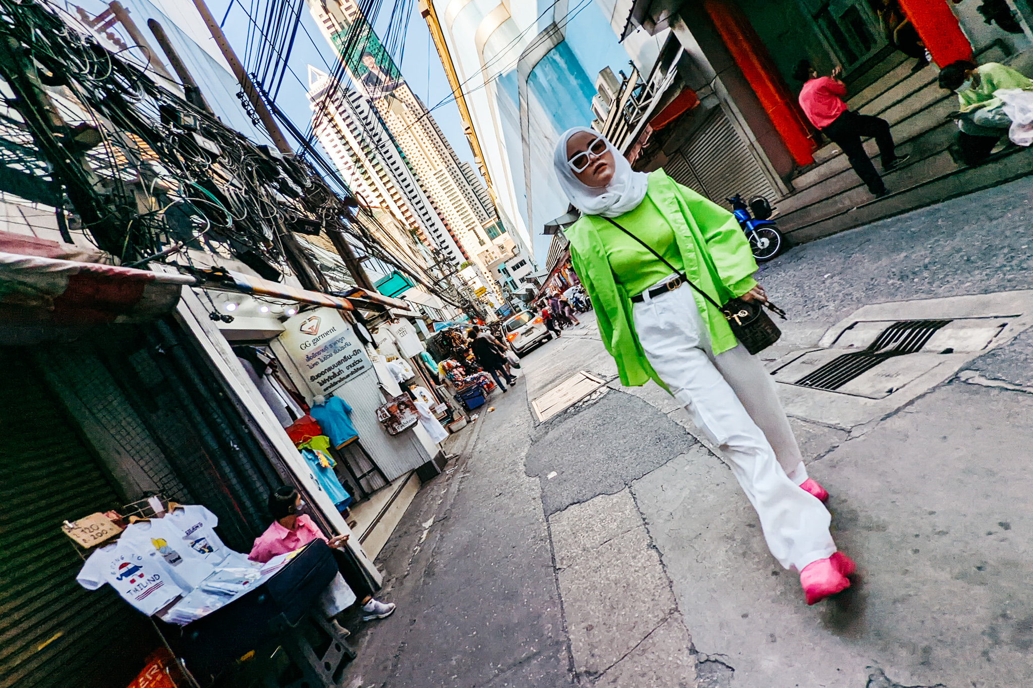 Woman in bright green jacket and white pants walking down a Bangkok street.