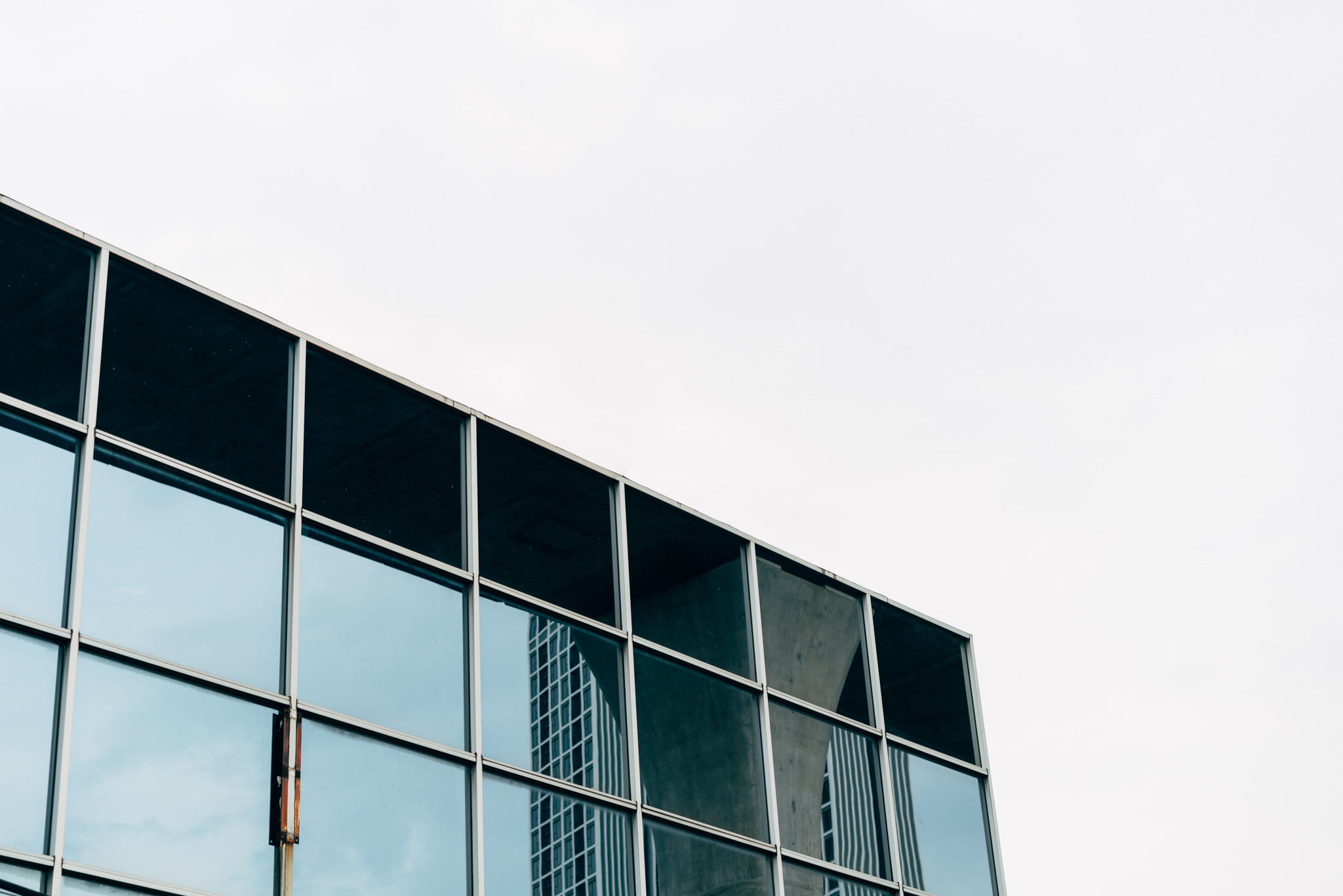 Low-angle view of a modern building's glass facade reflecting a nearby skyscraper.