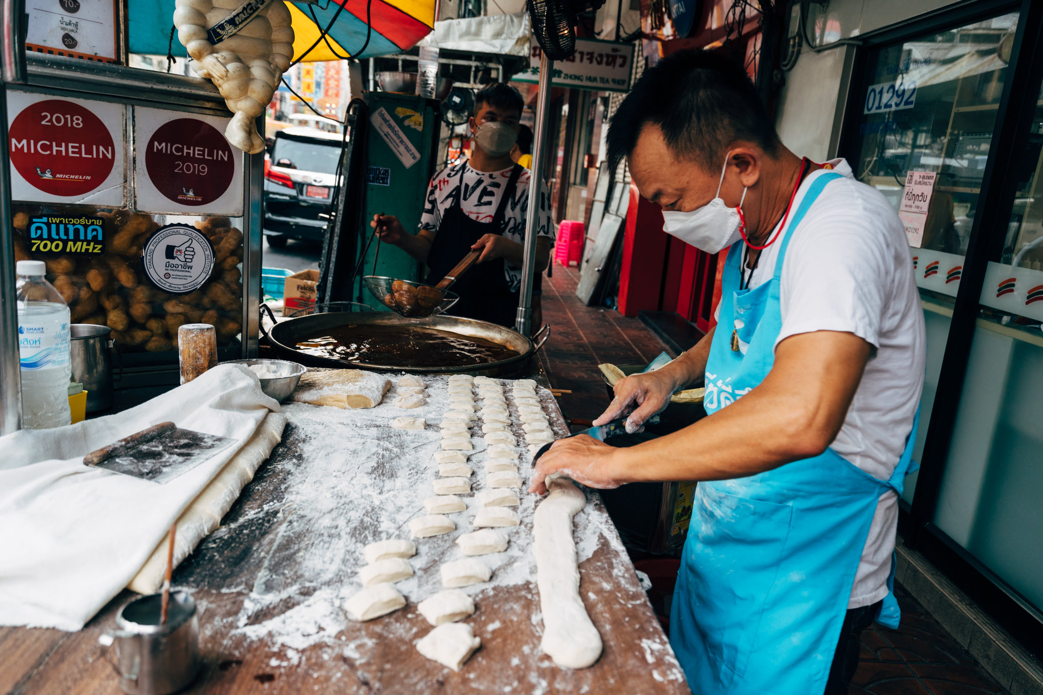 A street vendor in a facemask prepares dough for fried snacks at a Michelin-recommended market stall.