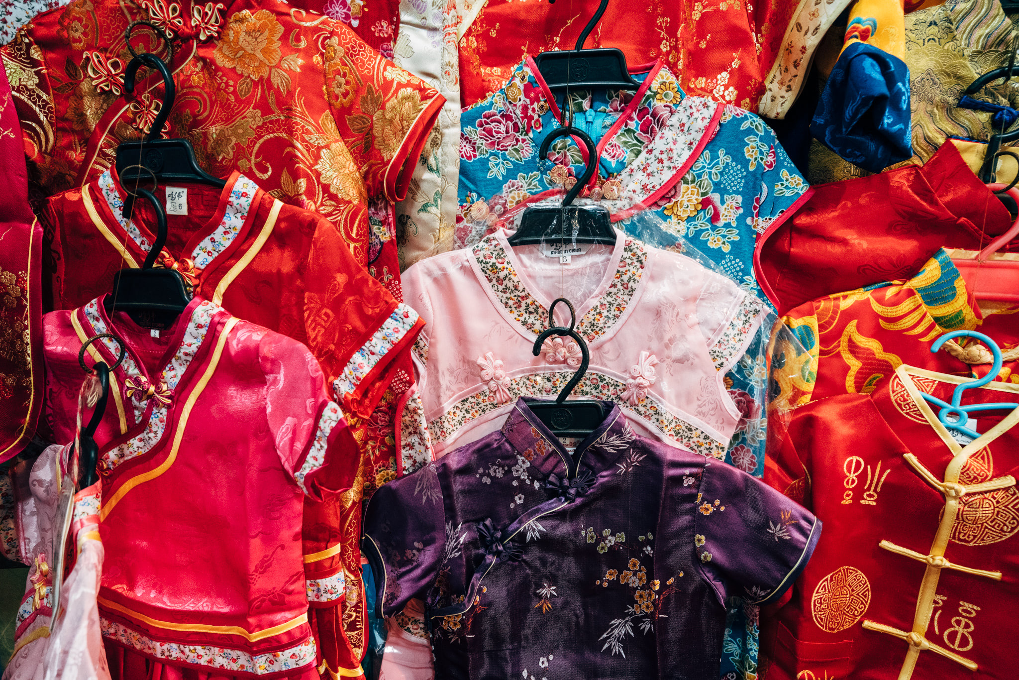 Close-up of several children's traditional Chinese shirts on hangers, in various colors and patterns.