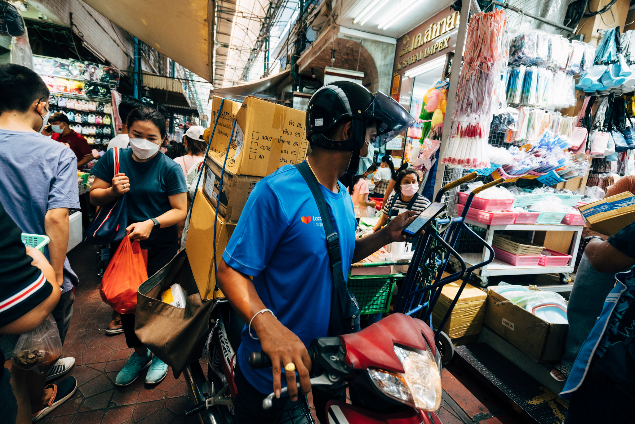 Delivery driver on motorbike in crowded market, carrying packages.