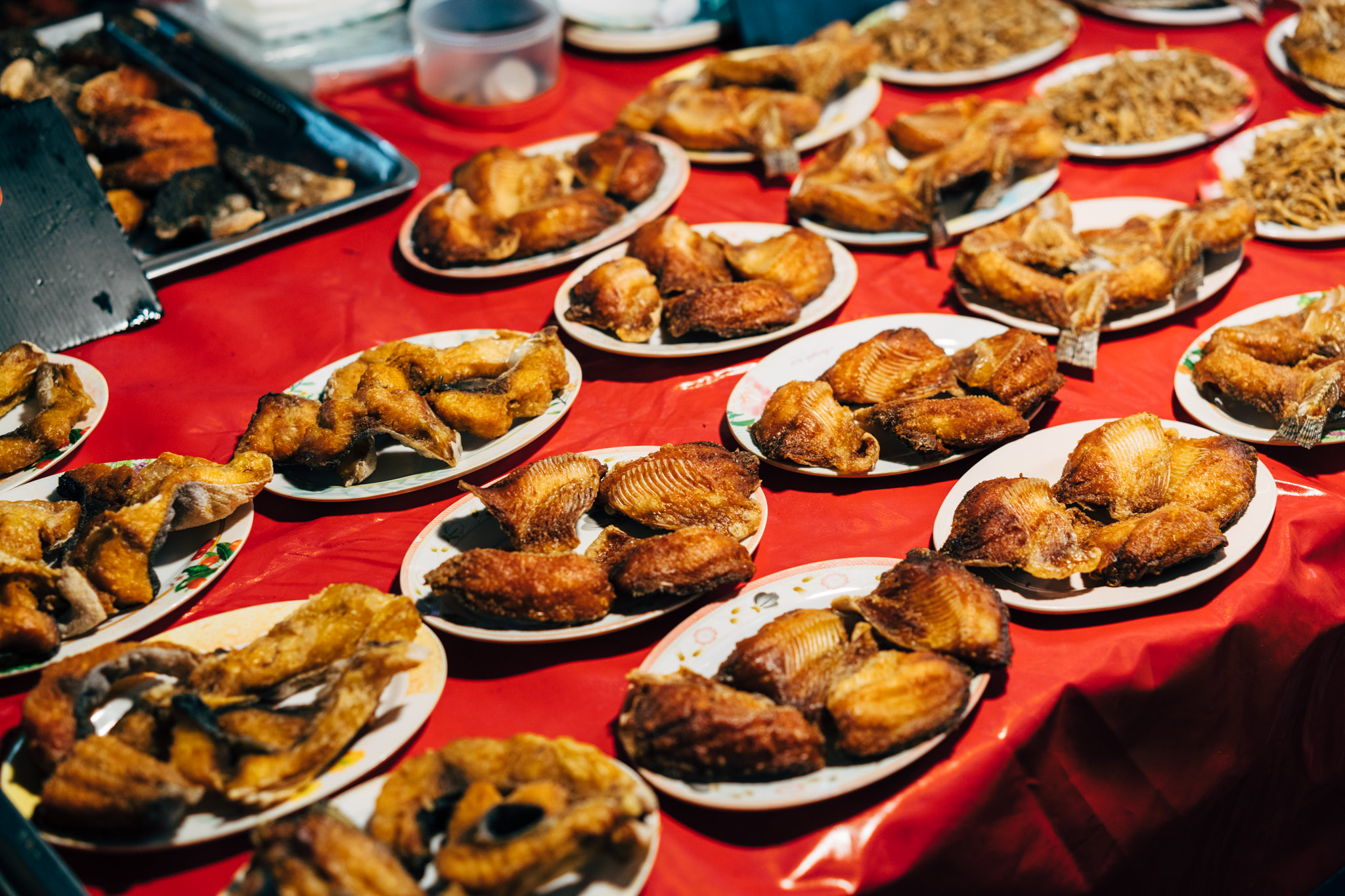 Many plates of fried fish on a red table at a market.