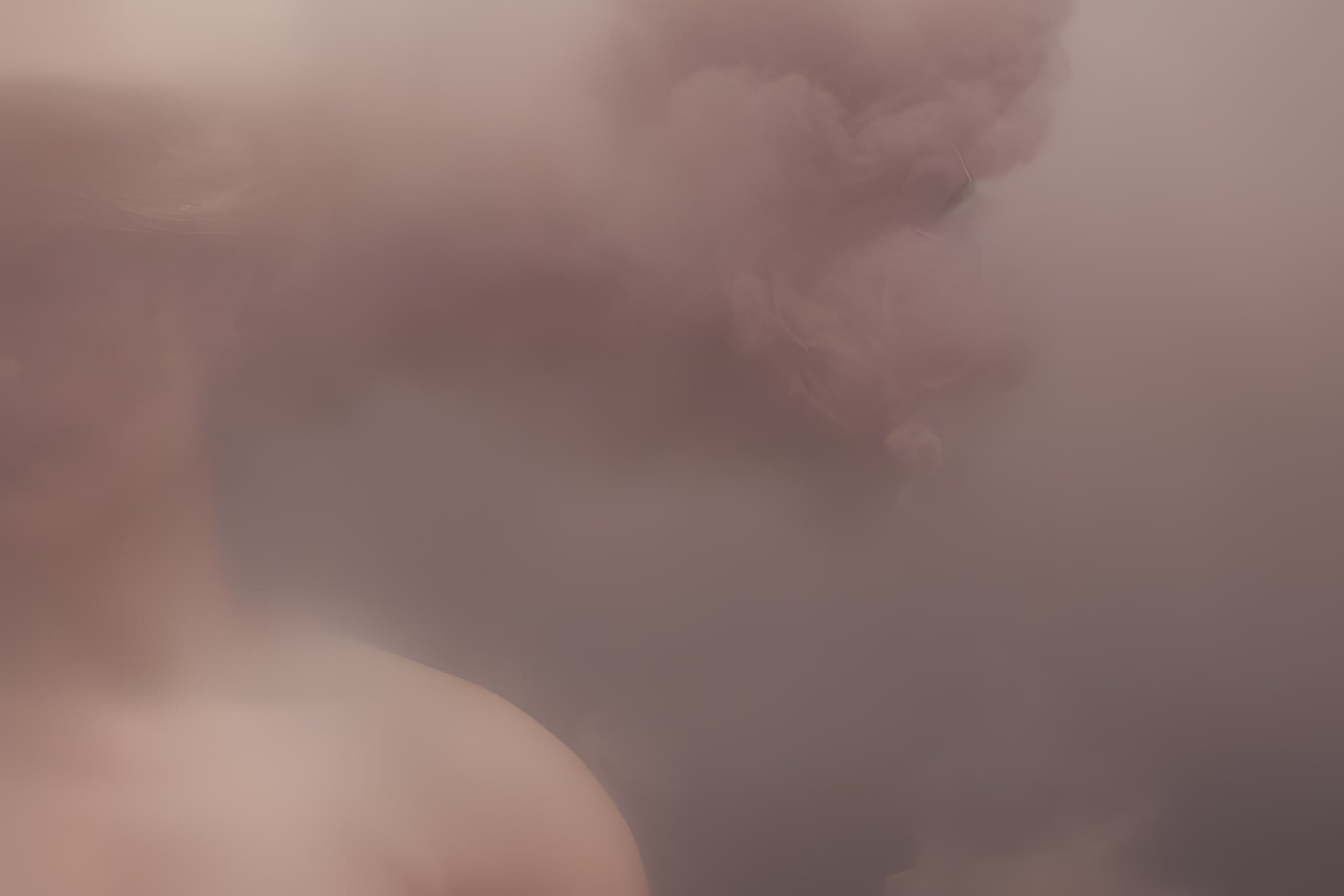Abstract image of a person's shoulder and neck obscured by pink smoke.