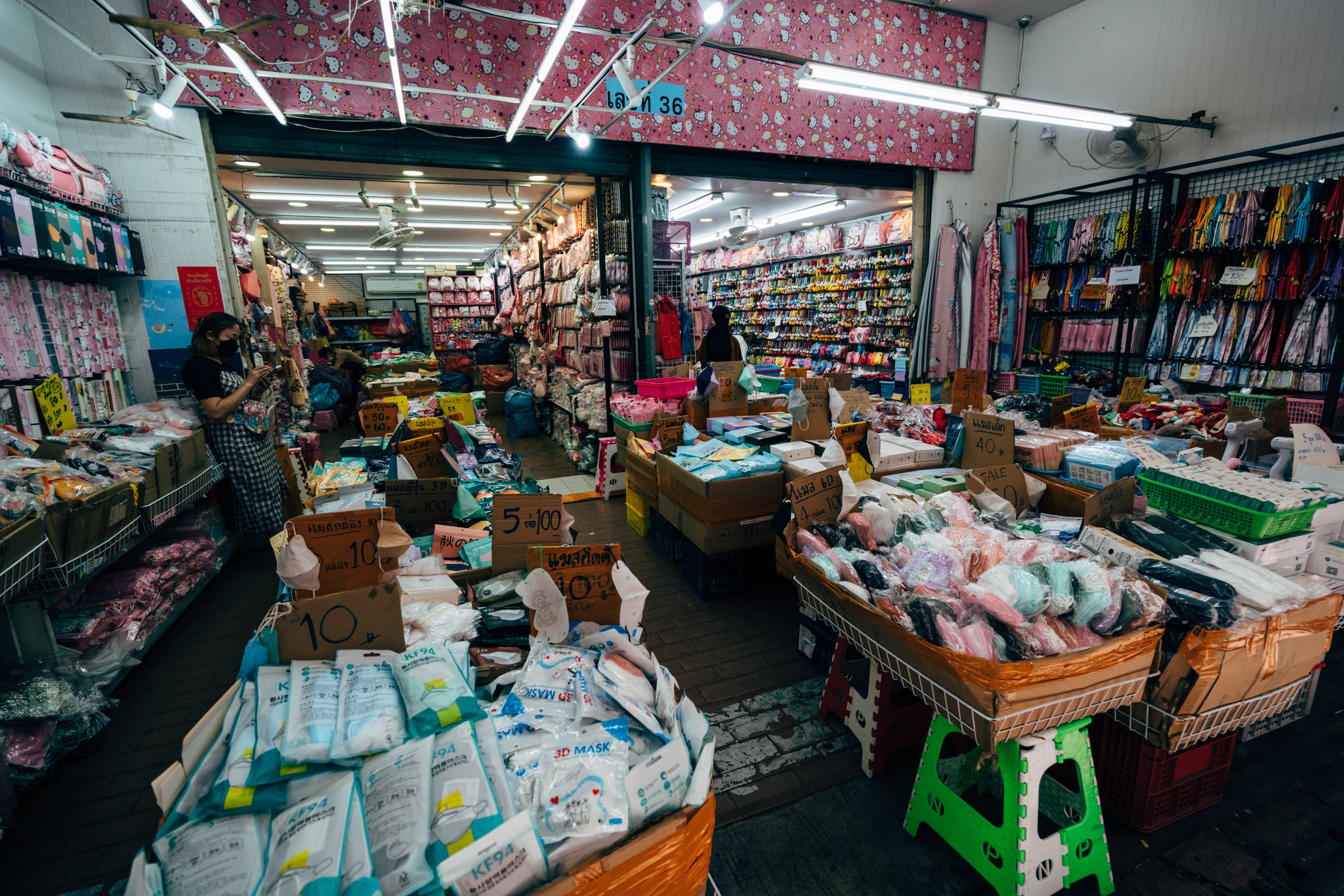A crowded Thai shopping district store overflowing with colorful merchandise, including face masks and other assorted goods.