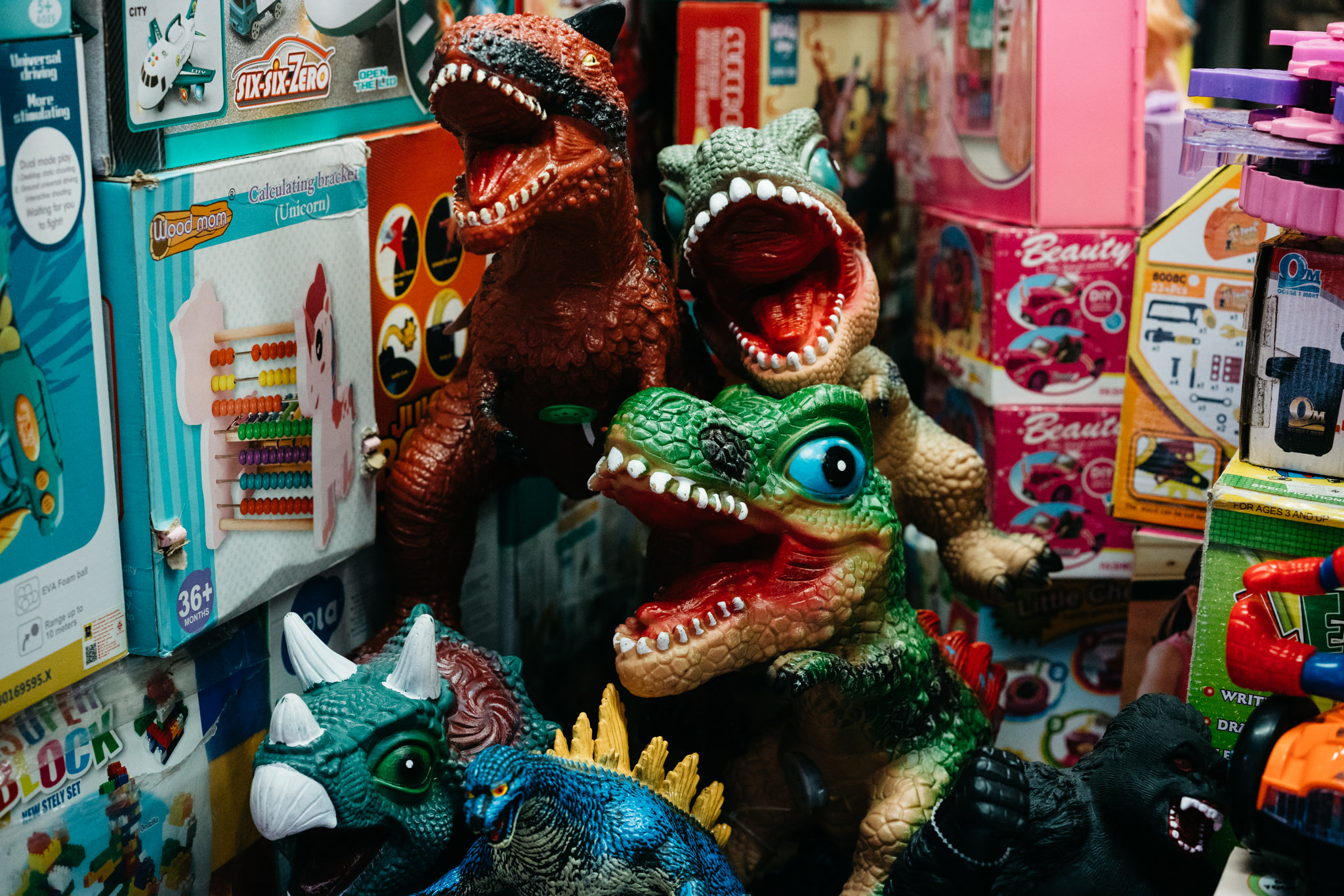 Several plastic dinosaur toys displayed amongst colorful toy packaging in a shop.