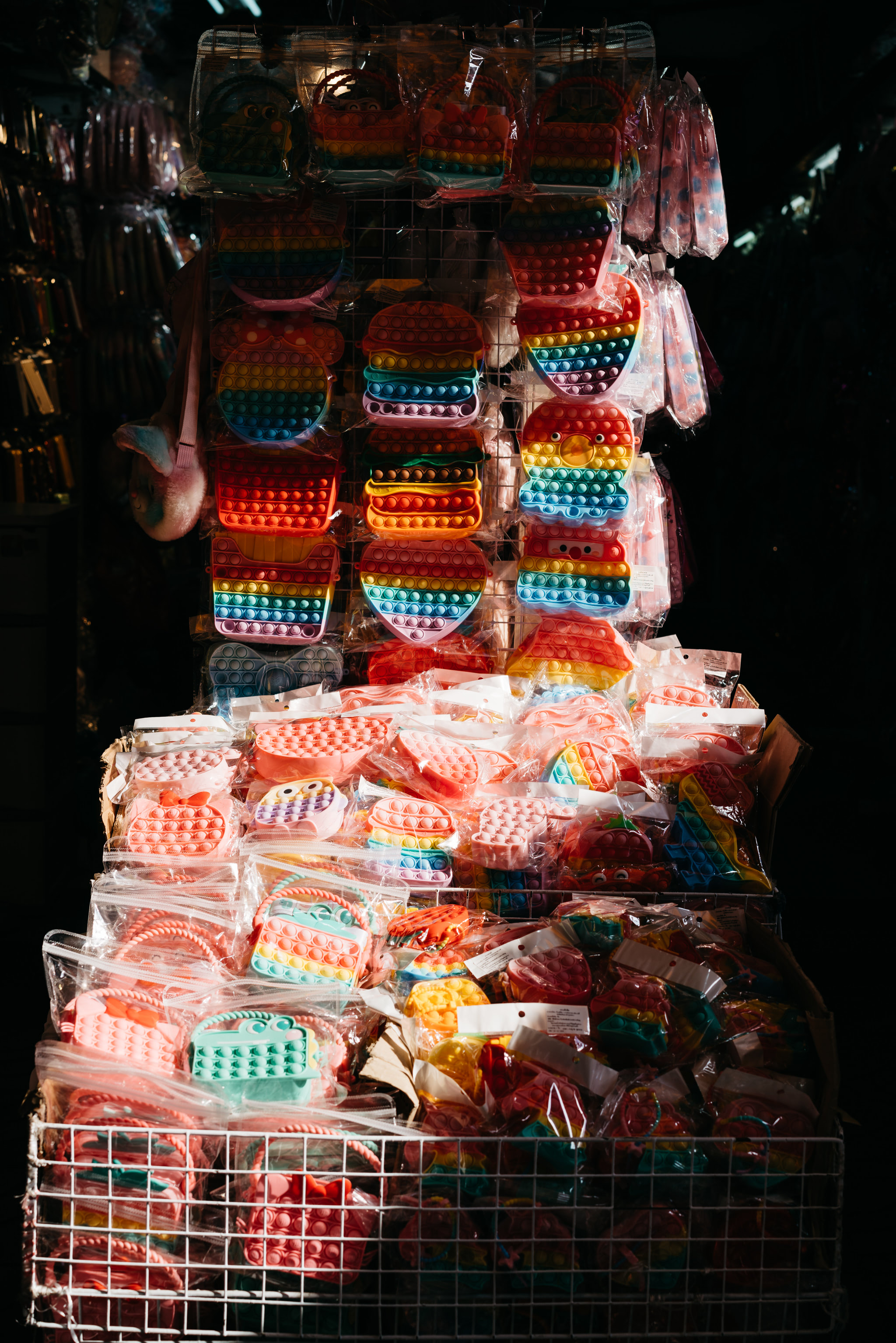 Many colorful pop-it toys in plastic packaging displayed on shelves and in a wire basket.
