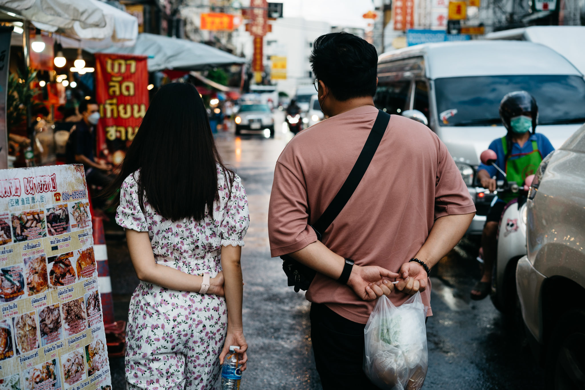 Rear view of a man and woman walking in a busy Thai shopping district.