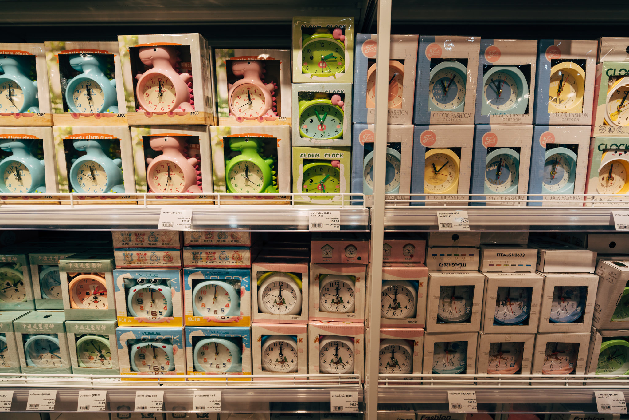 Shelf displaying various alarm clocks in boxes, many featuring cartoon dinosaur and animal designs.