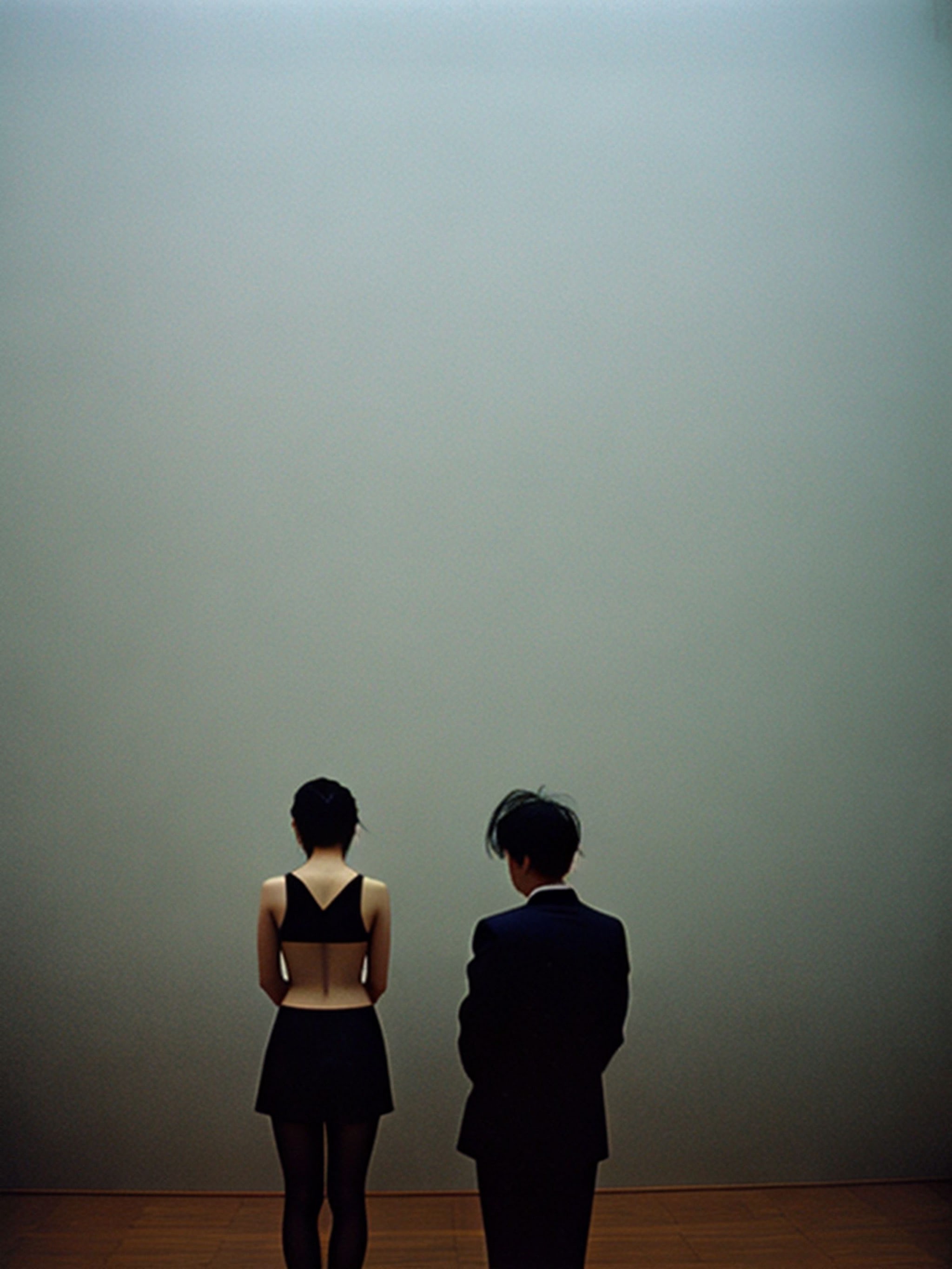 Couple viewed from behind standing before a large gray wall.