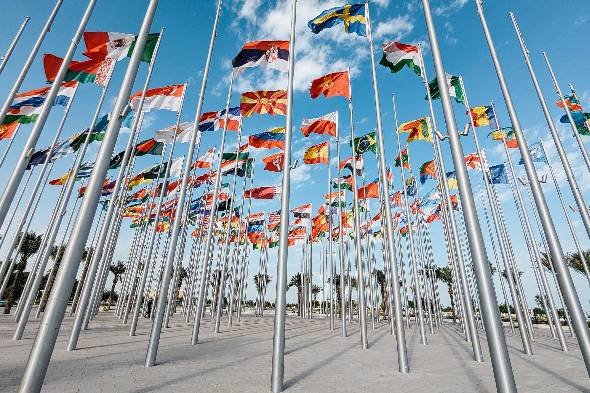 Many flags of various nations on tall silver poles, viewed from below against a blue sky.