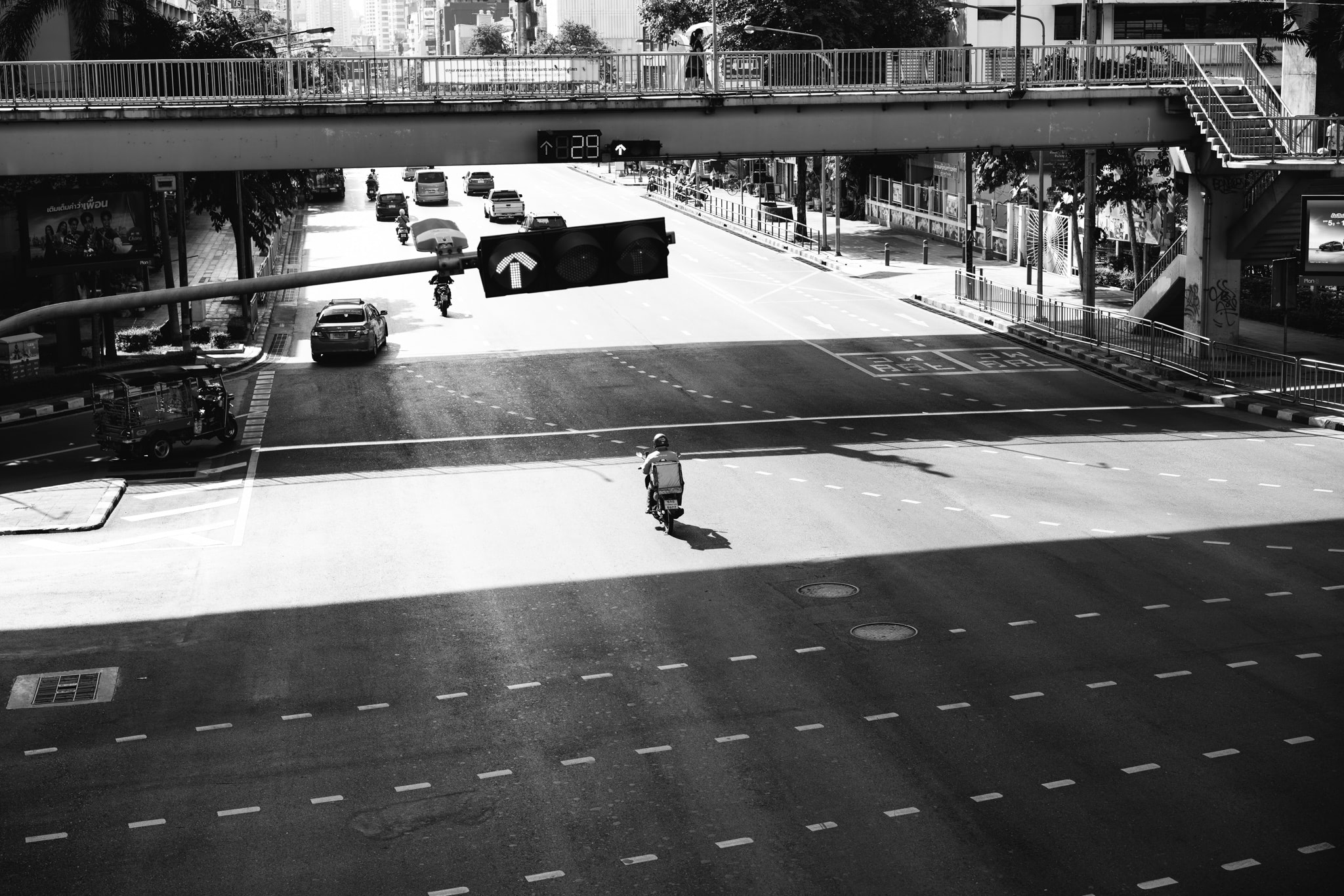 Black and white photo of a motorcyclist at an intersection under a bridge.