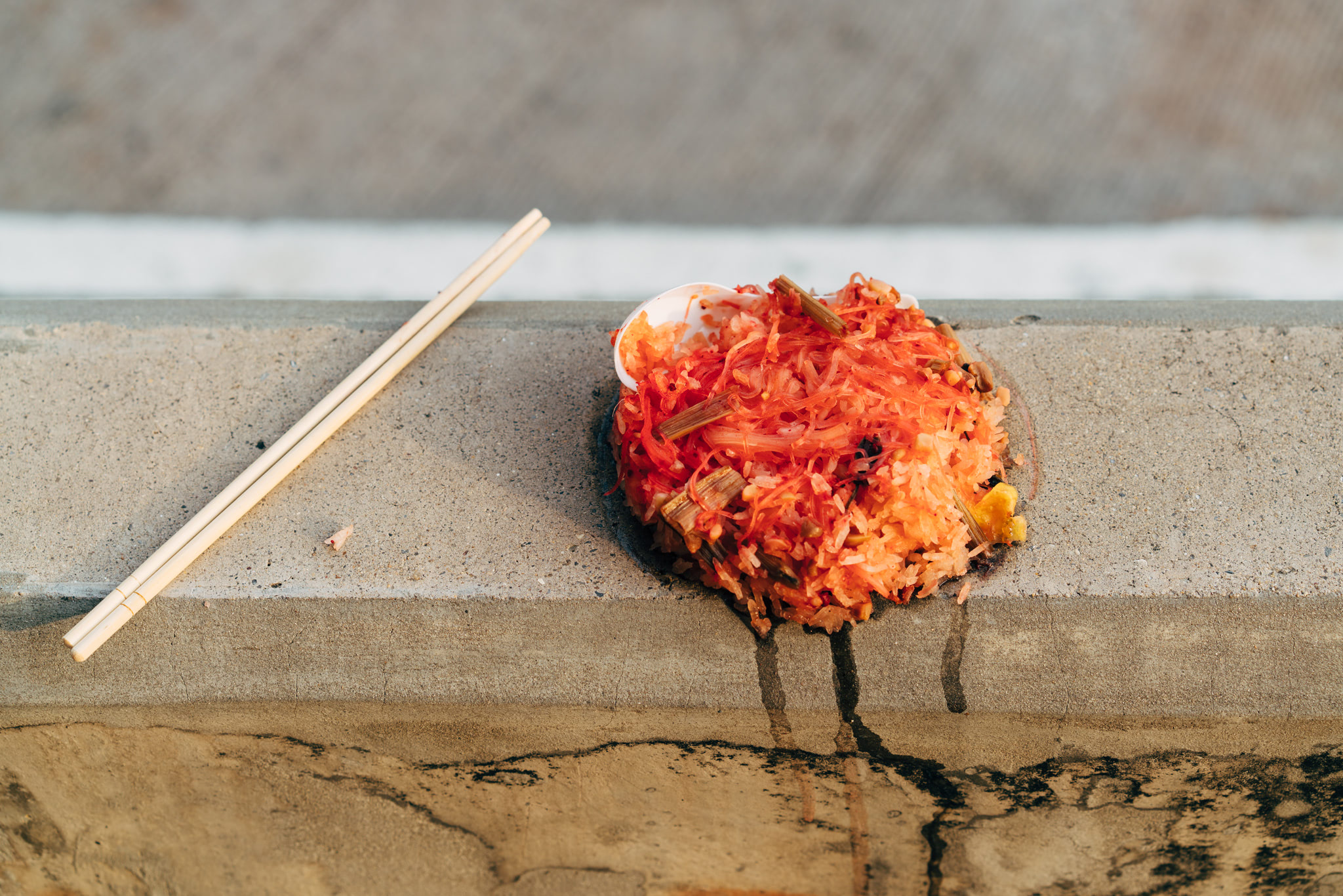 Leftover red rice dish spilled on concrete with chopsticks nearby.