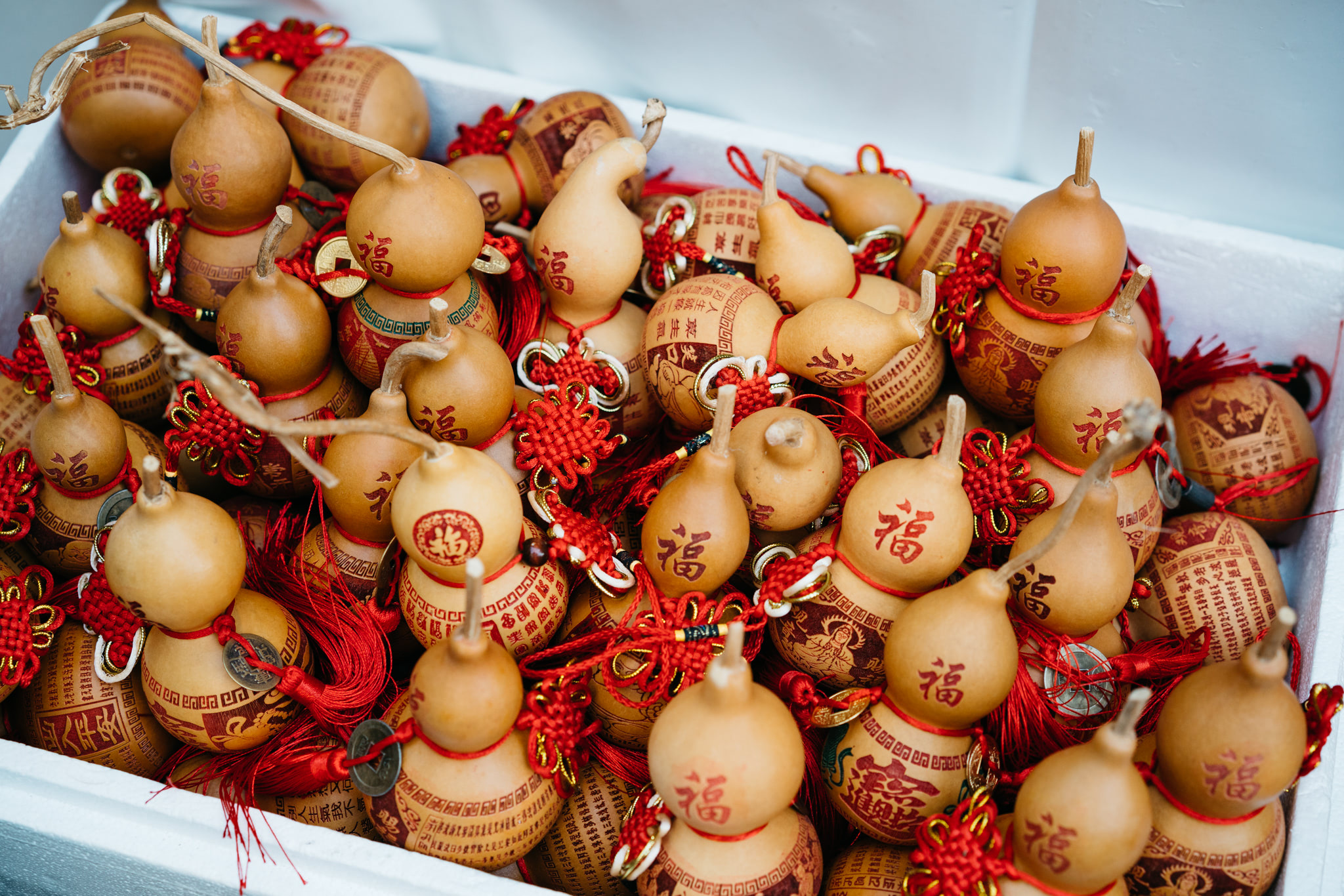 Many small, light-brown Chinese gourds with red Chinese characters and red tassels.