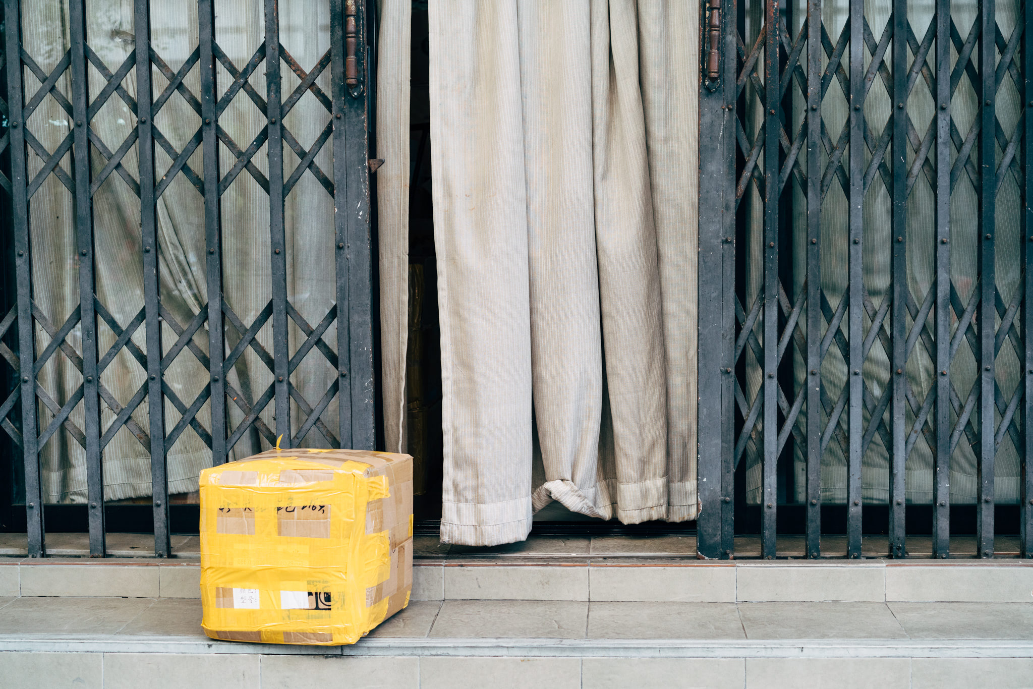 Package sitting on steps in front of a doorway with a security gate and curtain.