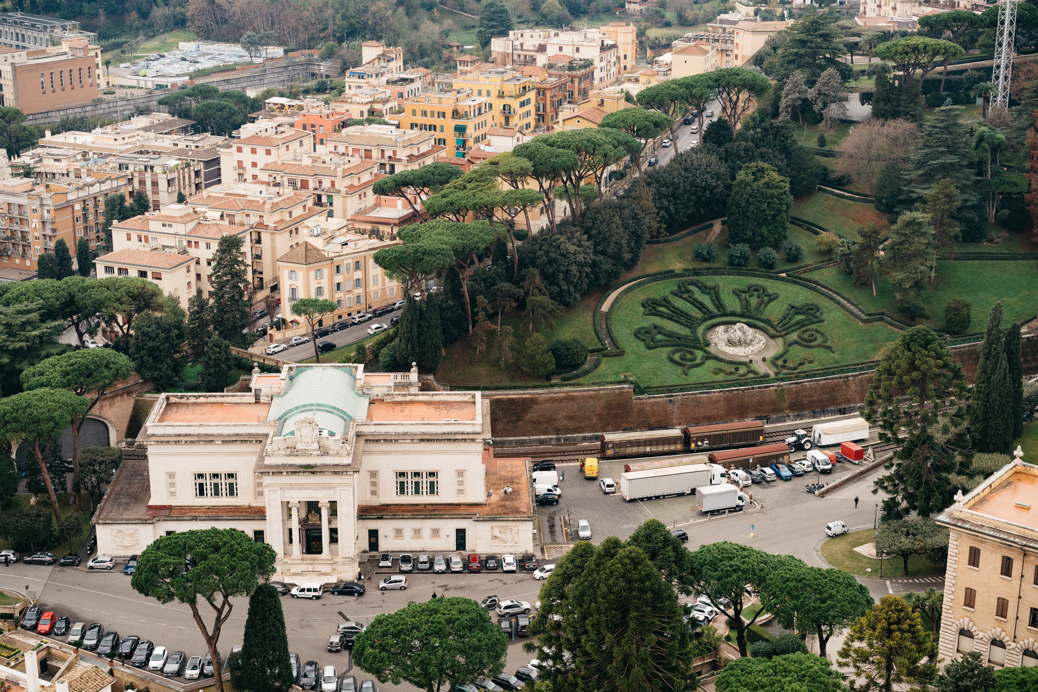 Aerial view of Rome, showing buildings, a park with a fountain, and a train station.