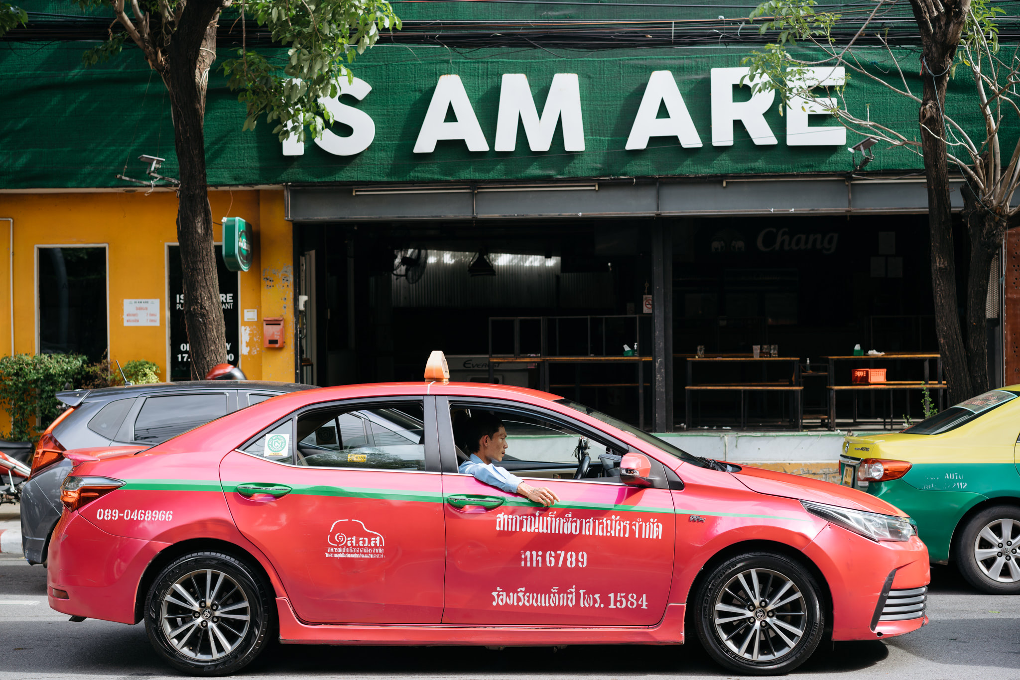 Pink Bangkok taxi parked on city street.