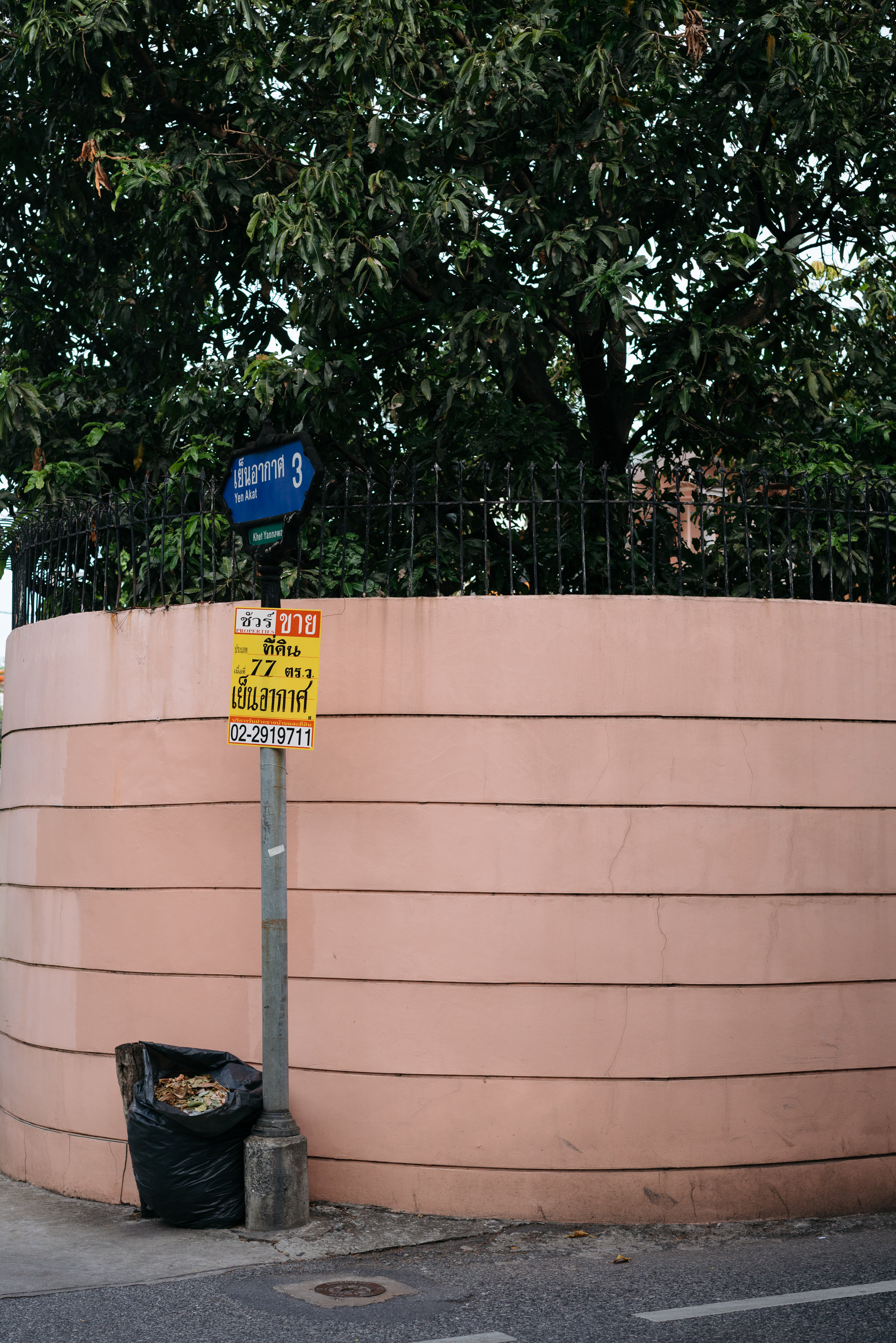Bus stop sign in Bangkok with Thai text and a black garbage bag.