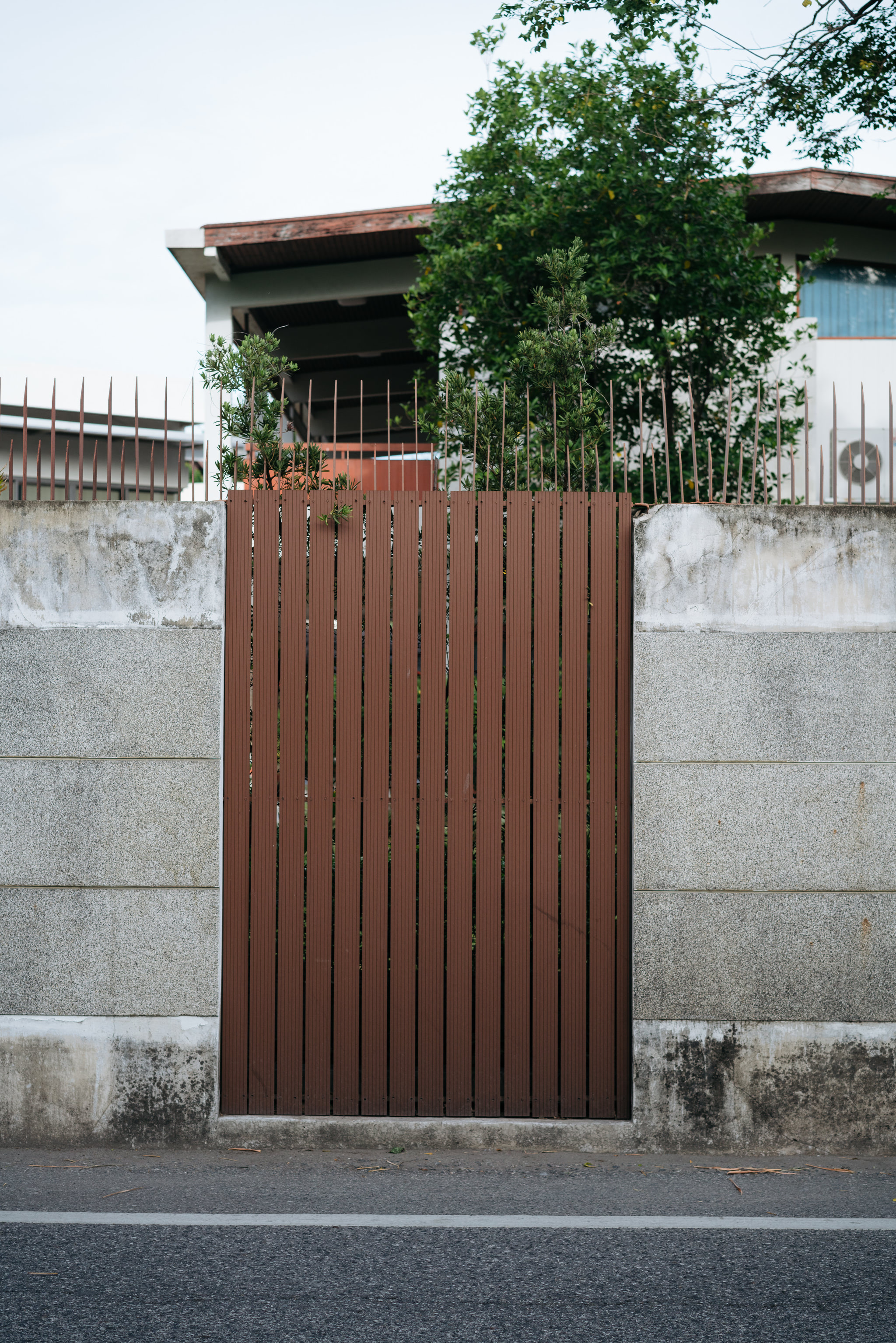 Brown gate in a gray concrete wall topped with rusty spikes.