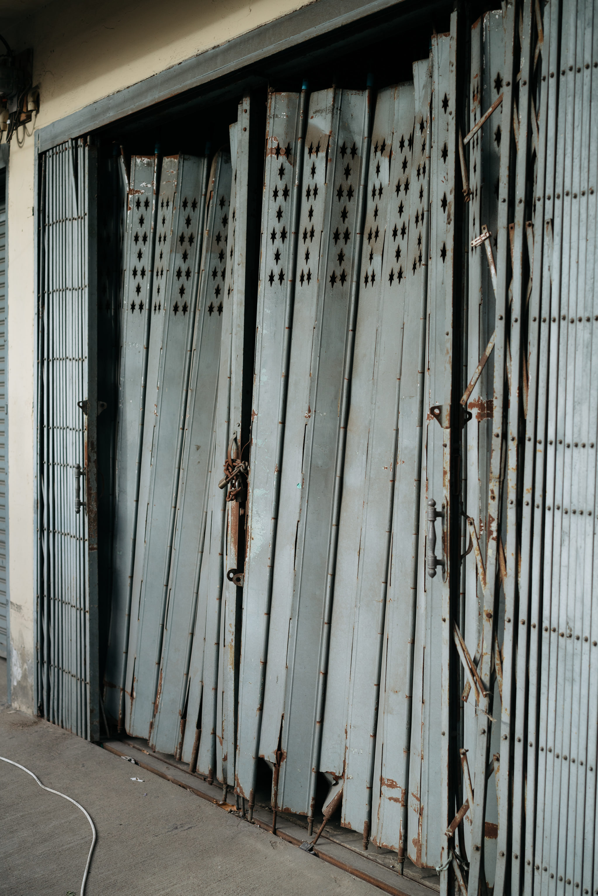 Rusty, gray metal folding gate with star-shaped cutouts, partially open and damaged.