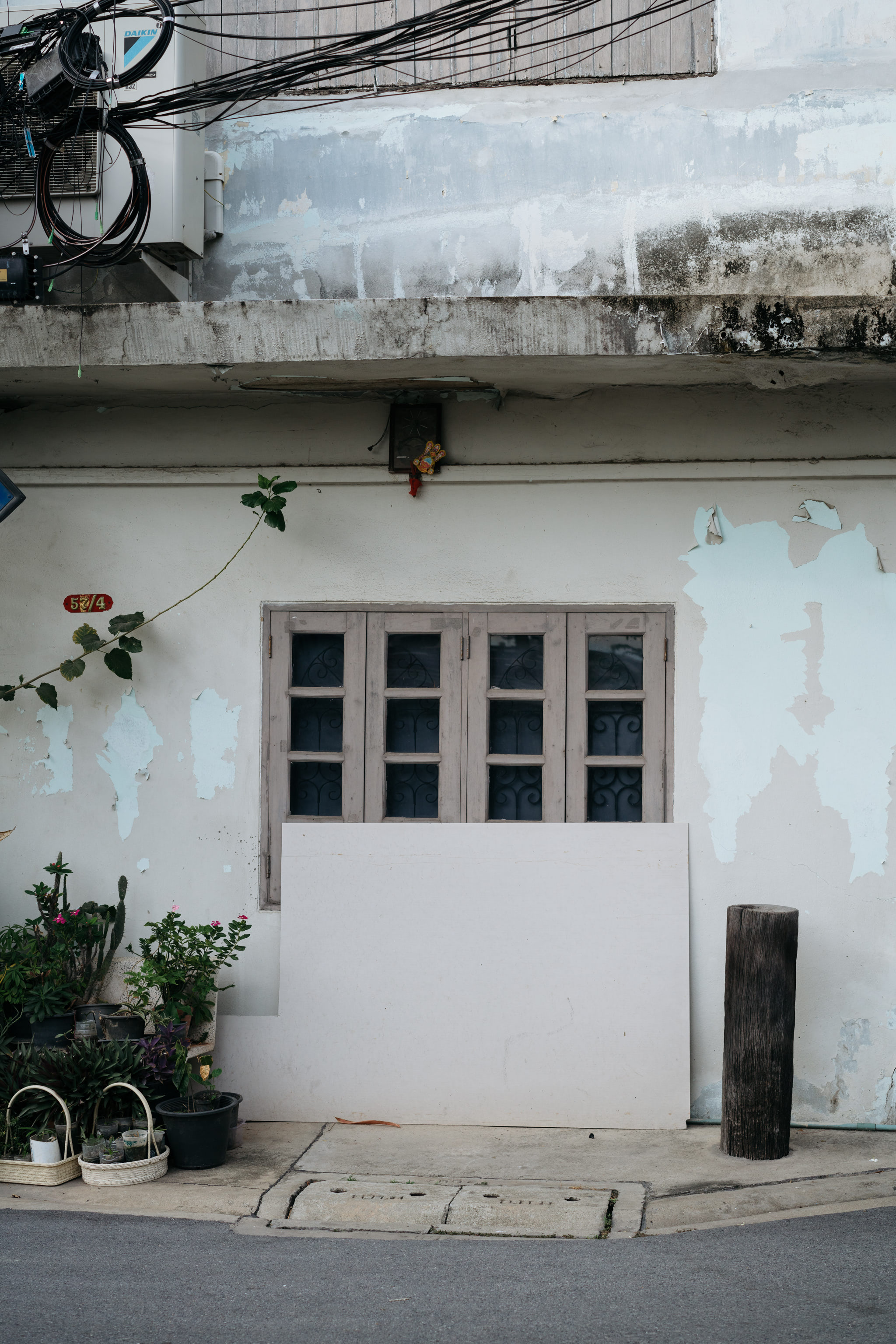 Distressed building facade with plants, a covered window, and a blank board.