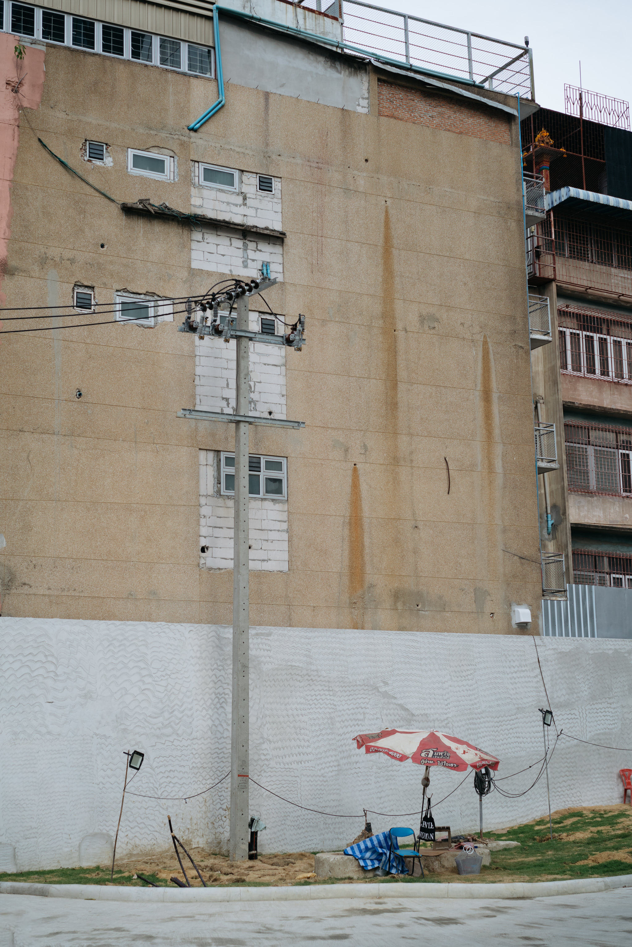 A weathered tan building with a utility pole and a small vendor's stall with a red and white umbrella in front.