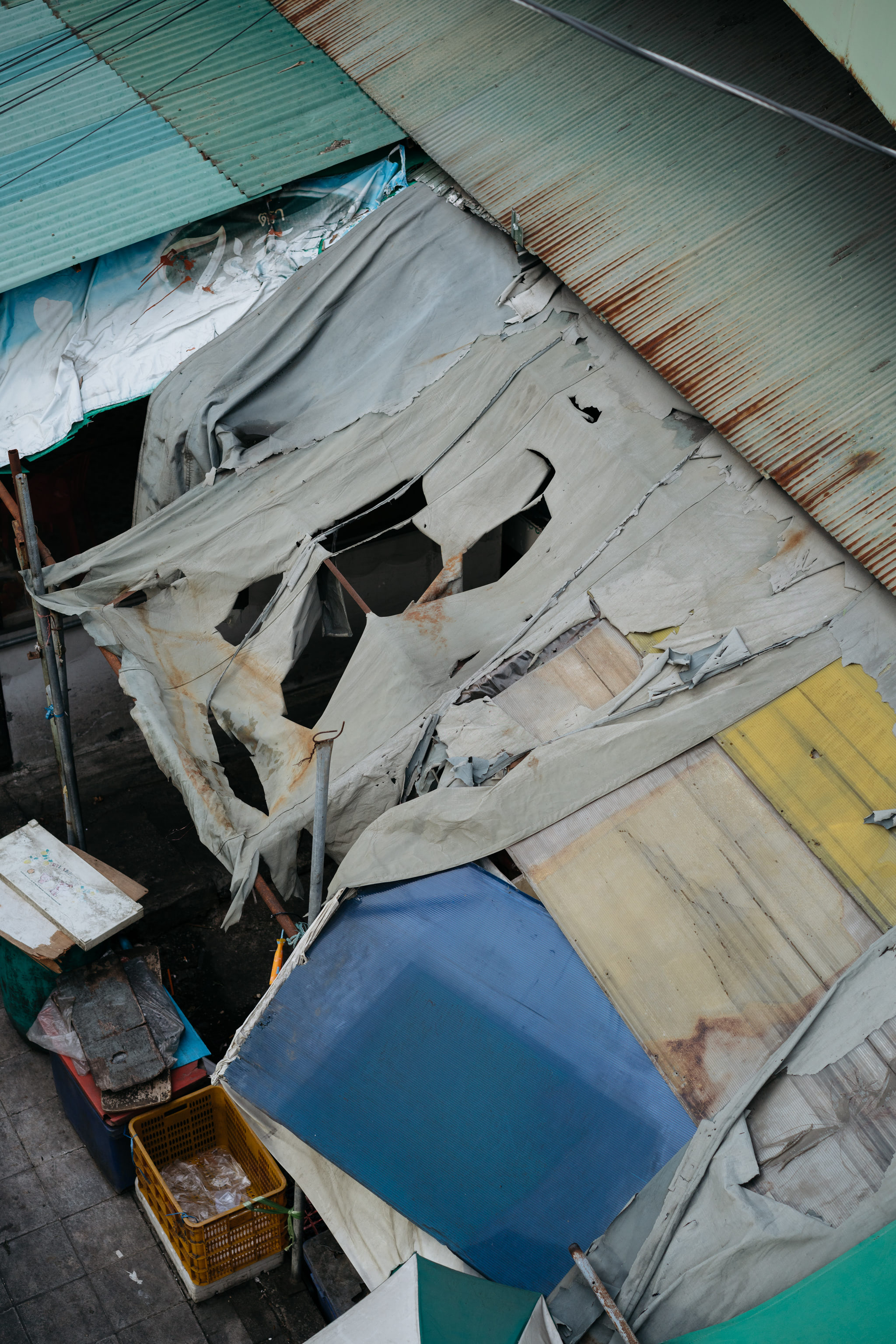 Overhead view of a dilapidated structure with torn tarps and rusted metal roofing.