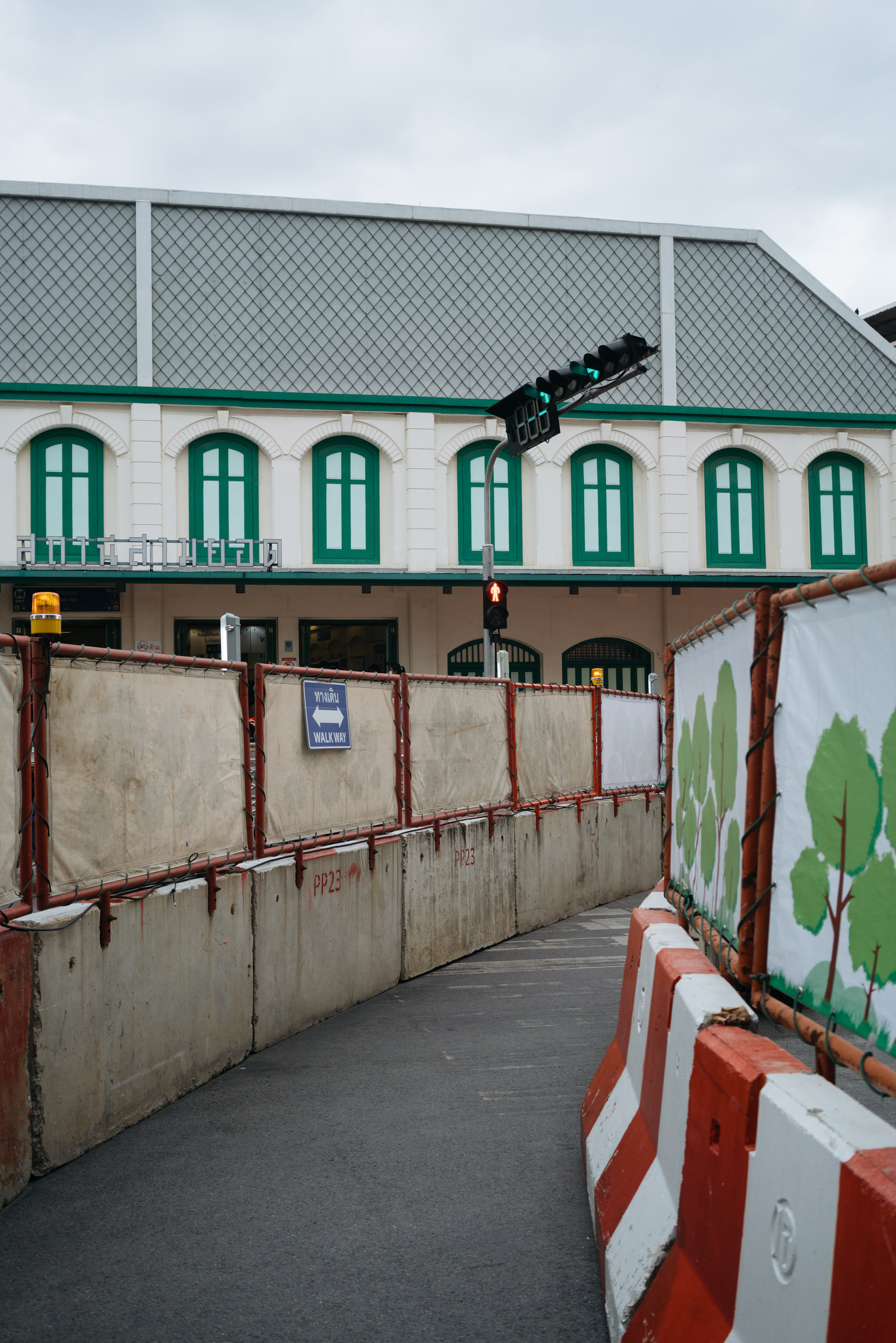 Construction site with concrete barriers and a pedestrian walkway sign in front of a building.