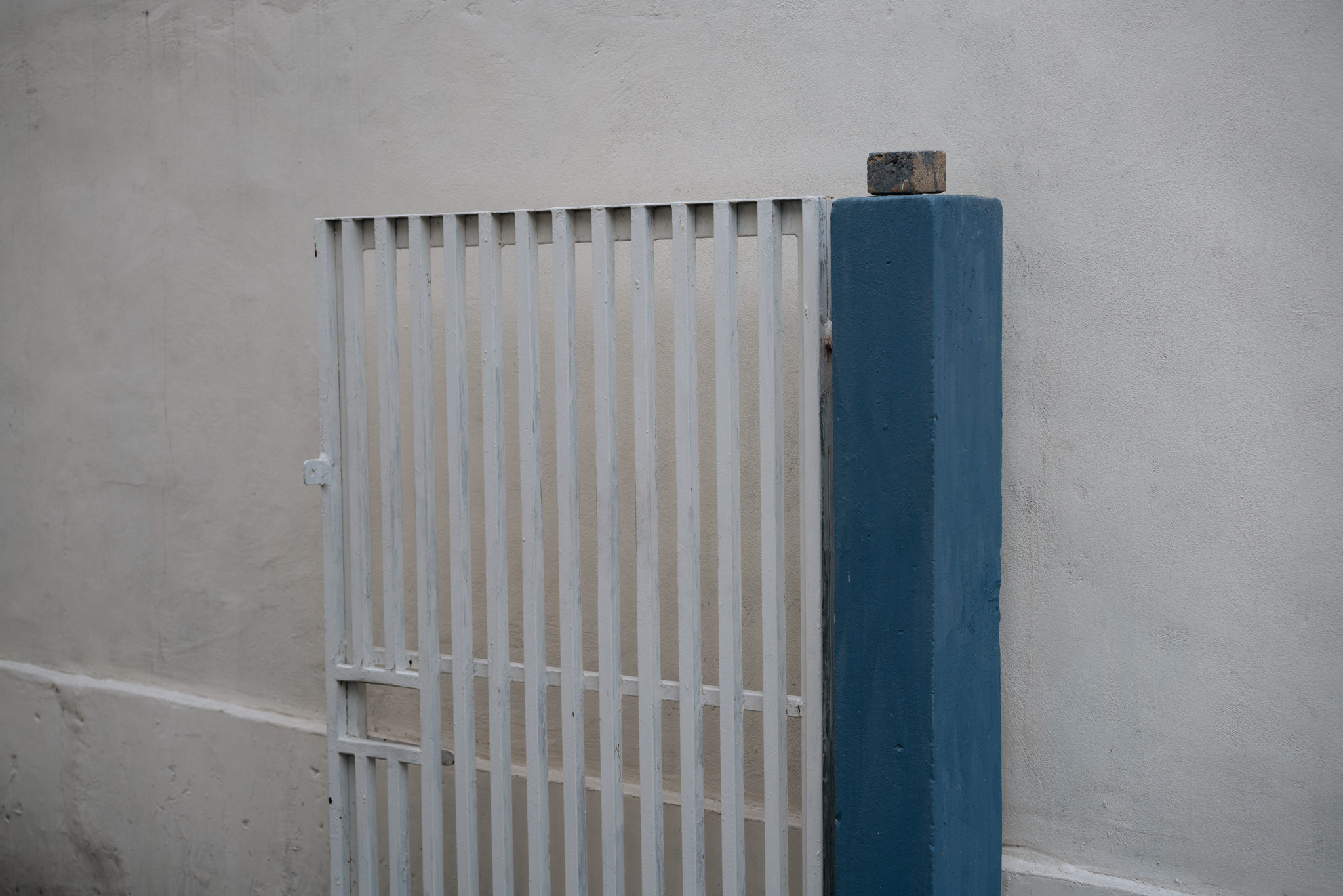 White metal gate against a beige wall with a blue post.