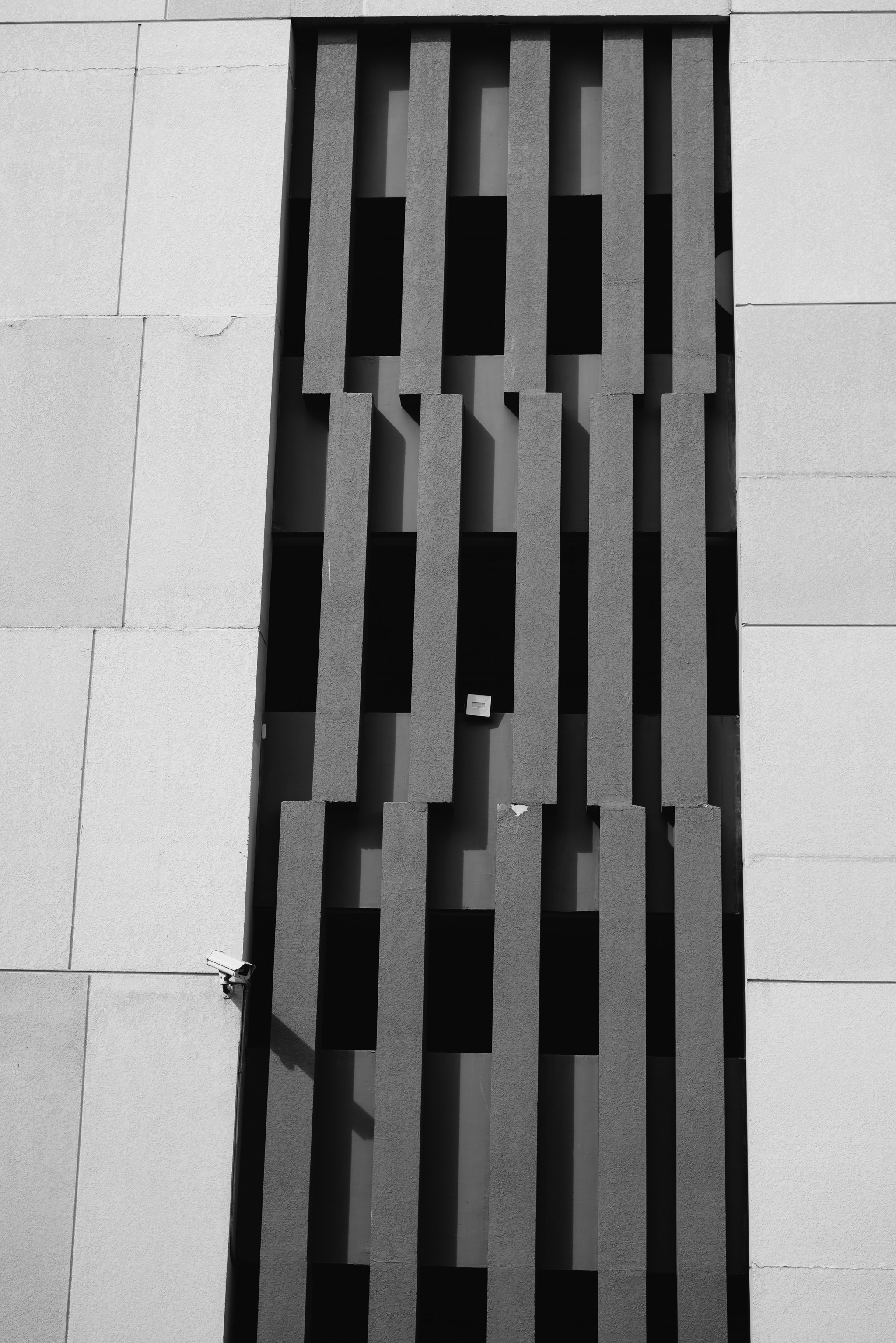 Black and white photo of a building's exterior, featuring a section of dark gray vertical slats set against a light gray wall.