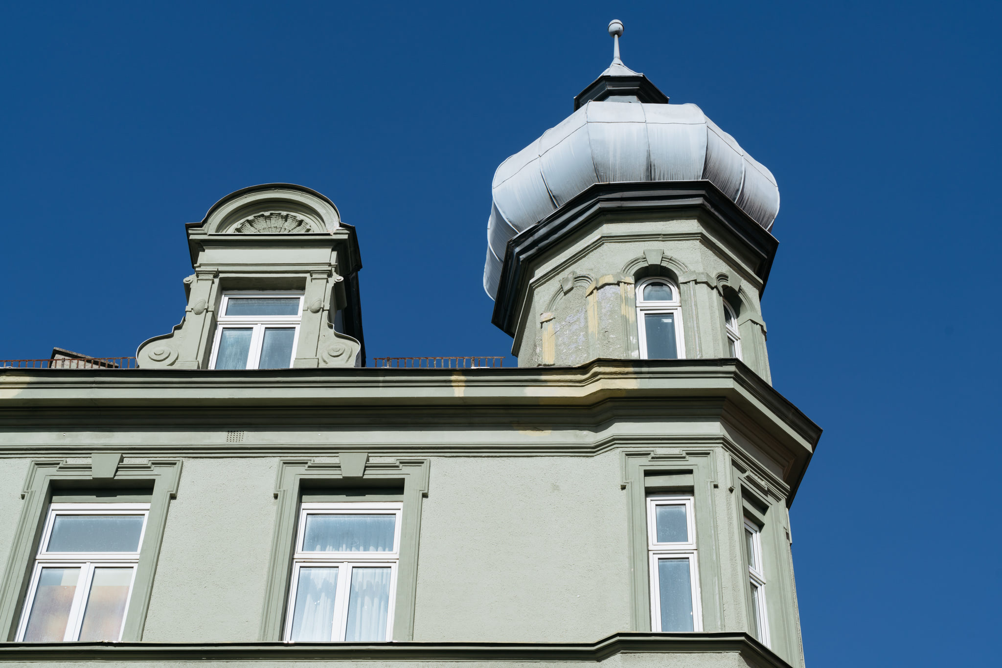 Green building with a cupola and ornate windows against a blue sky.